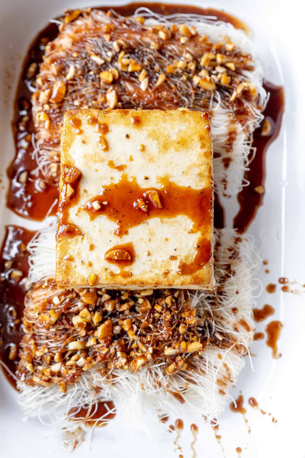 Tofu and noodles drizzled with brown sauce resting in a white casserole dish.