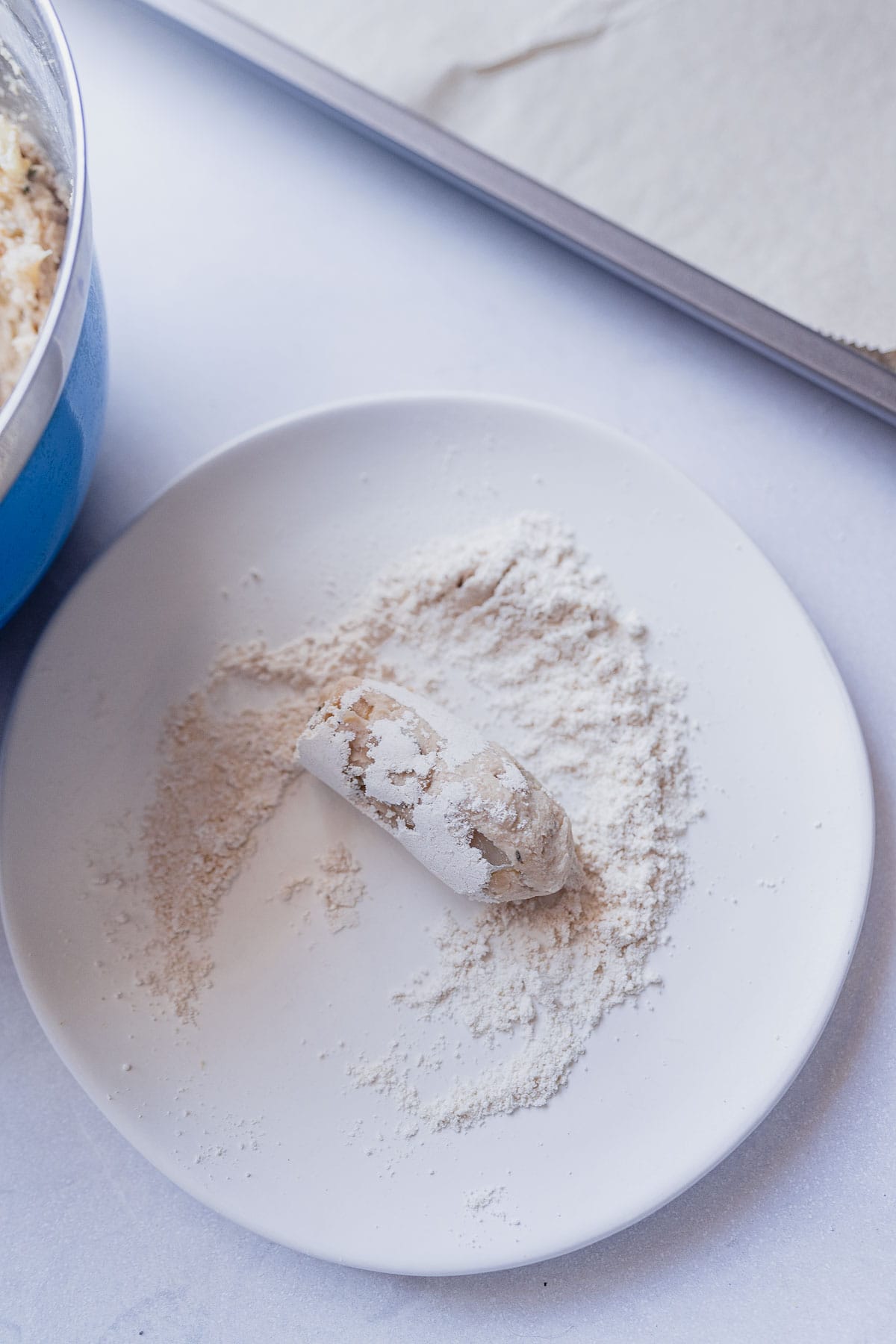 A white plate dusted with white flour with a rolled plant based sausage on it.