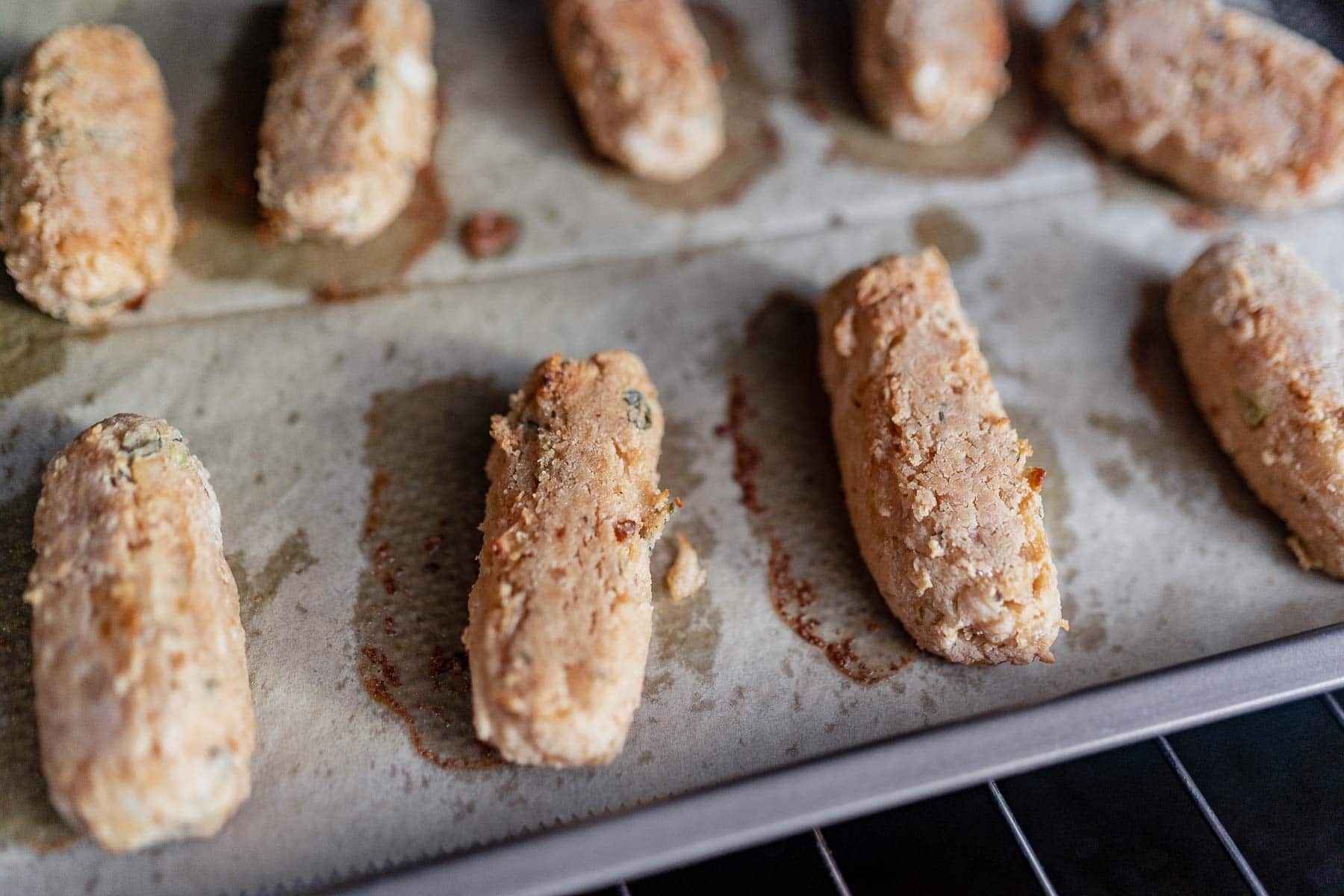 A baking sheet lined with parchment paper and topped with crispy cooked vegan sausages.