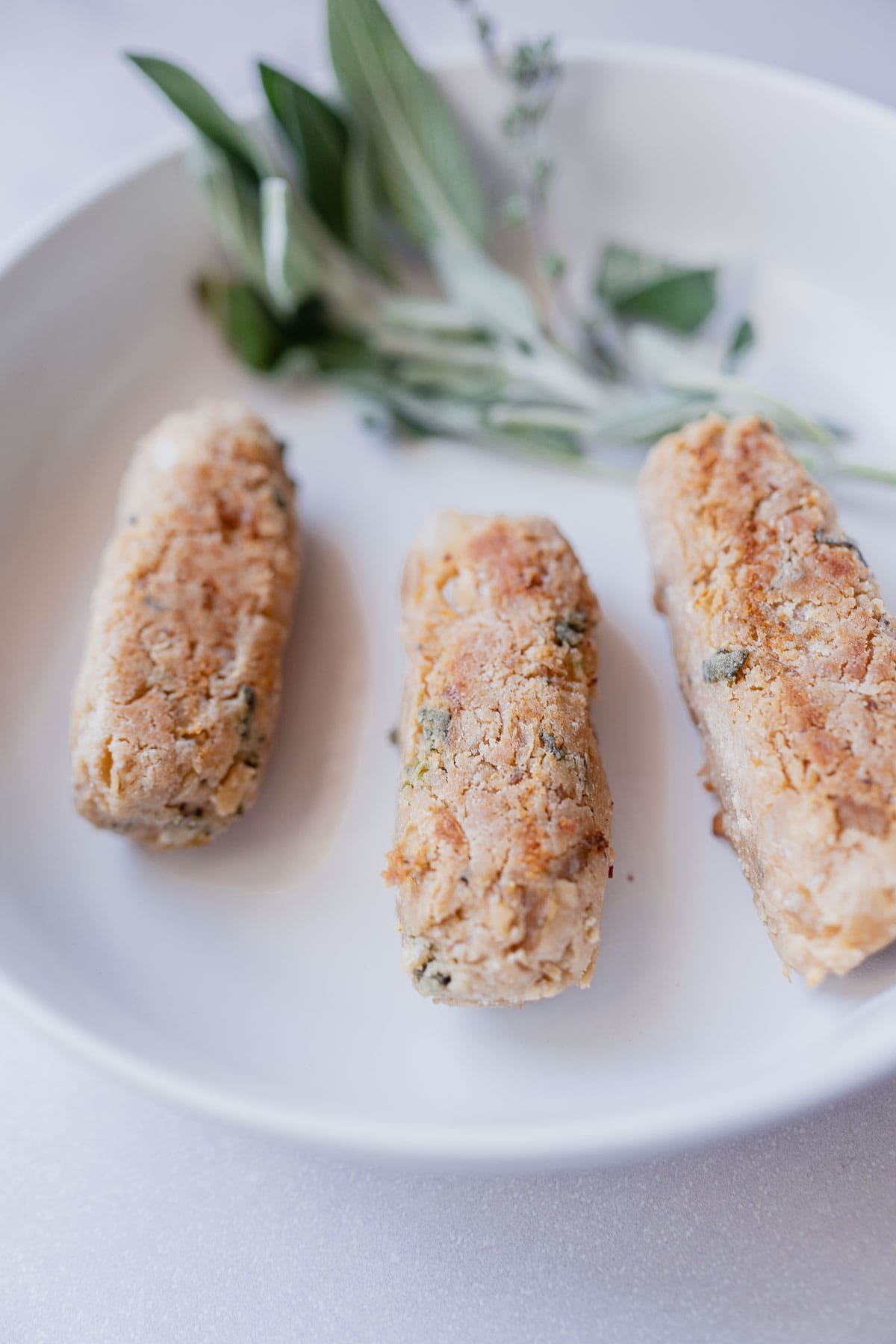 3 vegan sausages resting in a white ceramic bowl.