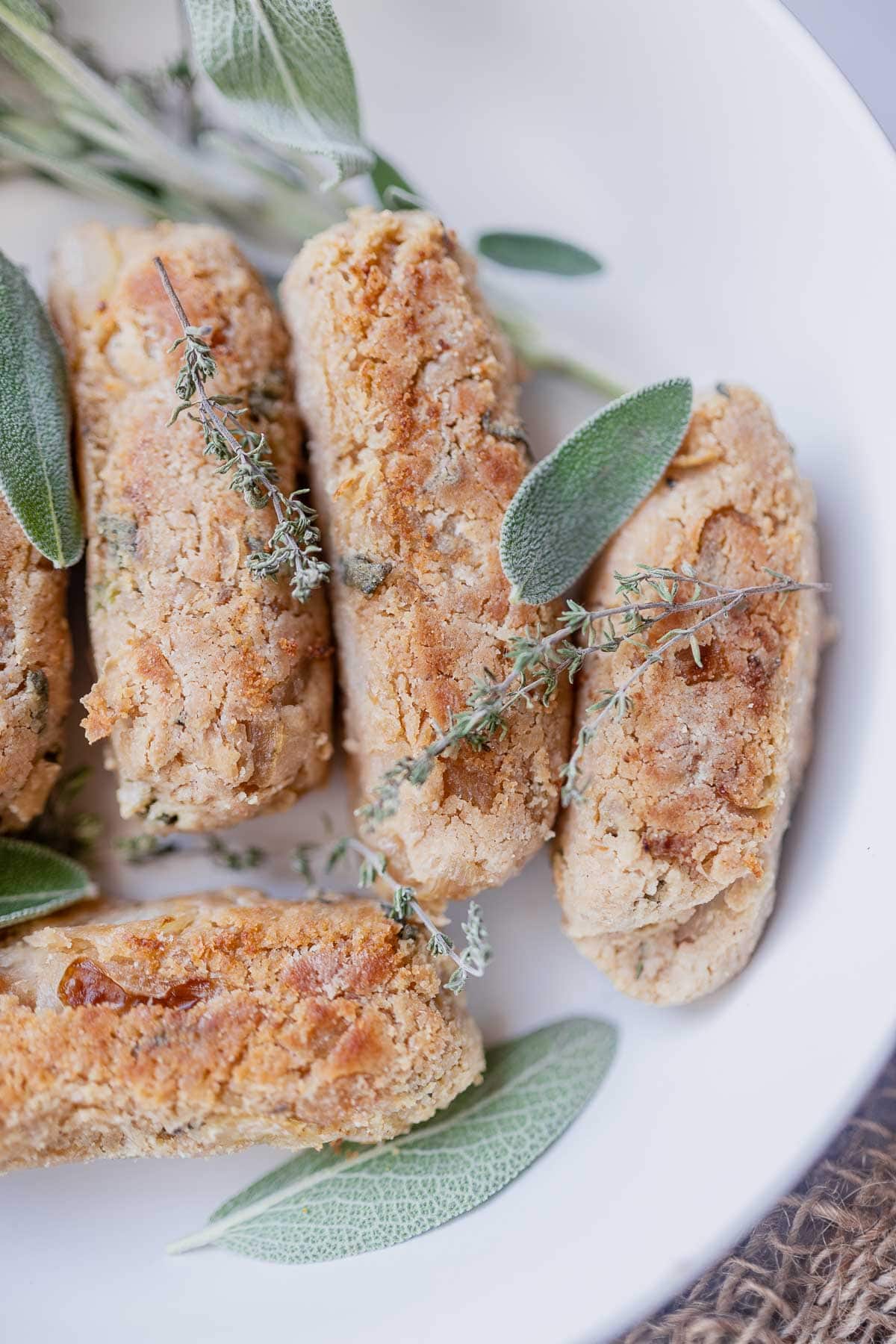 A close shot of plant based sausages in a white bowl topped with fresh green herbs.