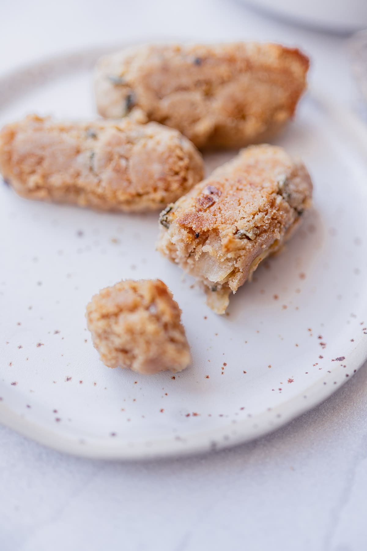 A vegan sausage that has been bitten into resting on a speckled ceramic plate.