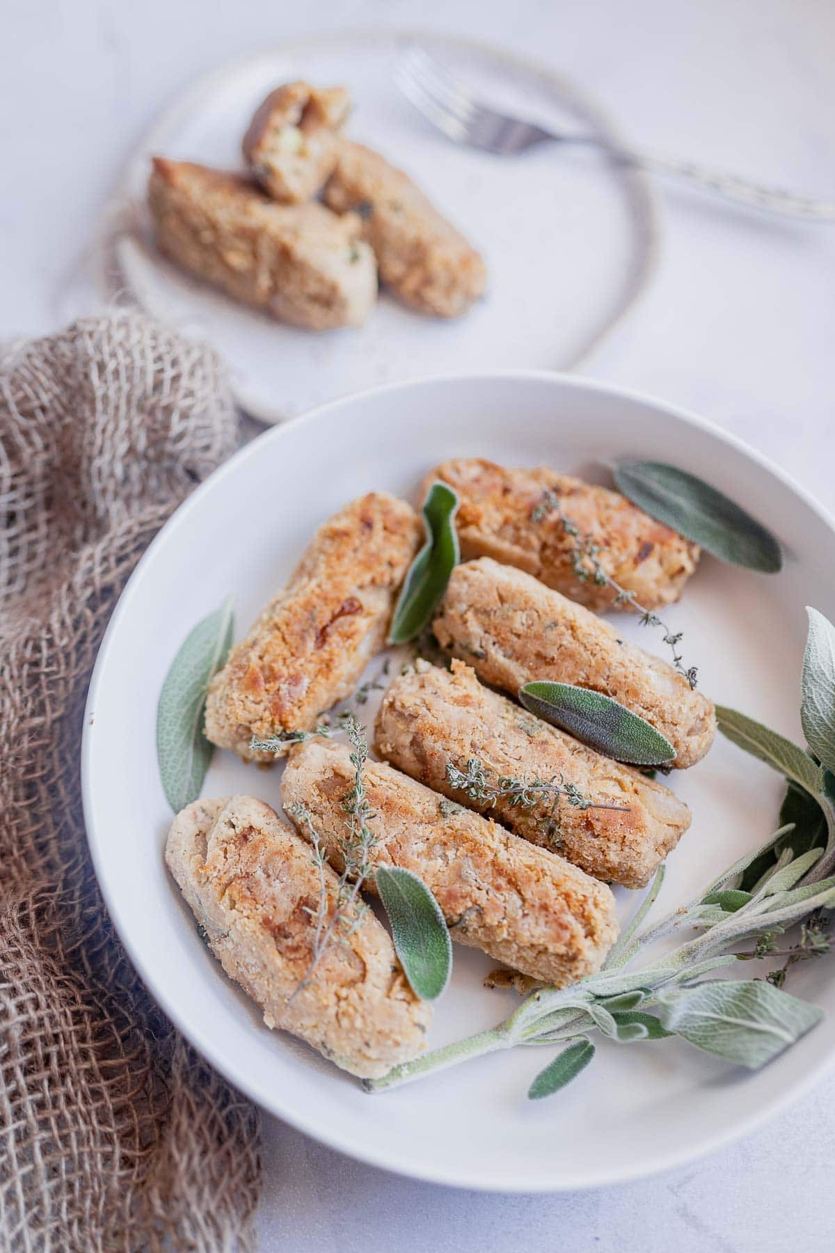 A white ceramic bowl filled with sausage and fresh herbs, resting on a burlap towel.