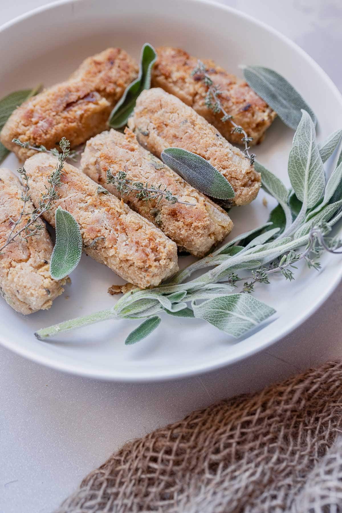 A shallow white ceramic bowl topped with golden sausages and fresh green herb leaves.