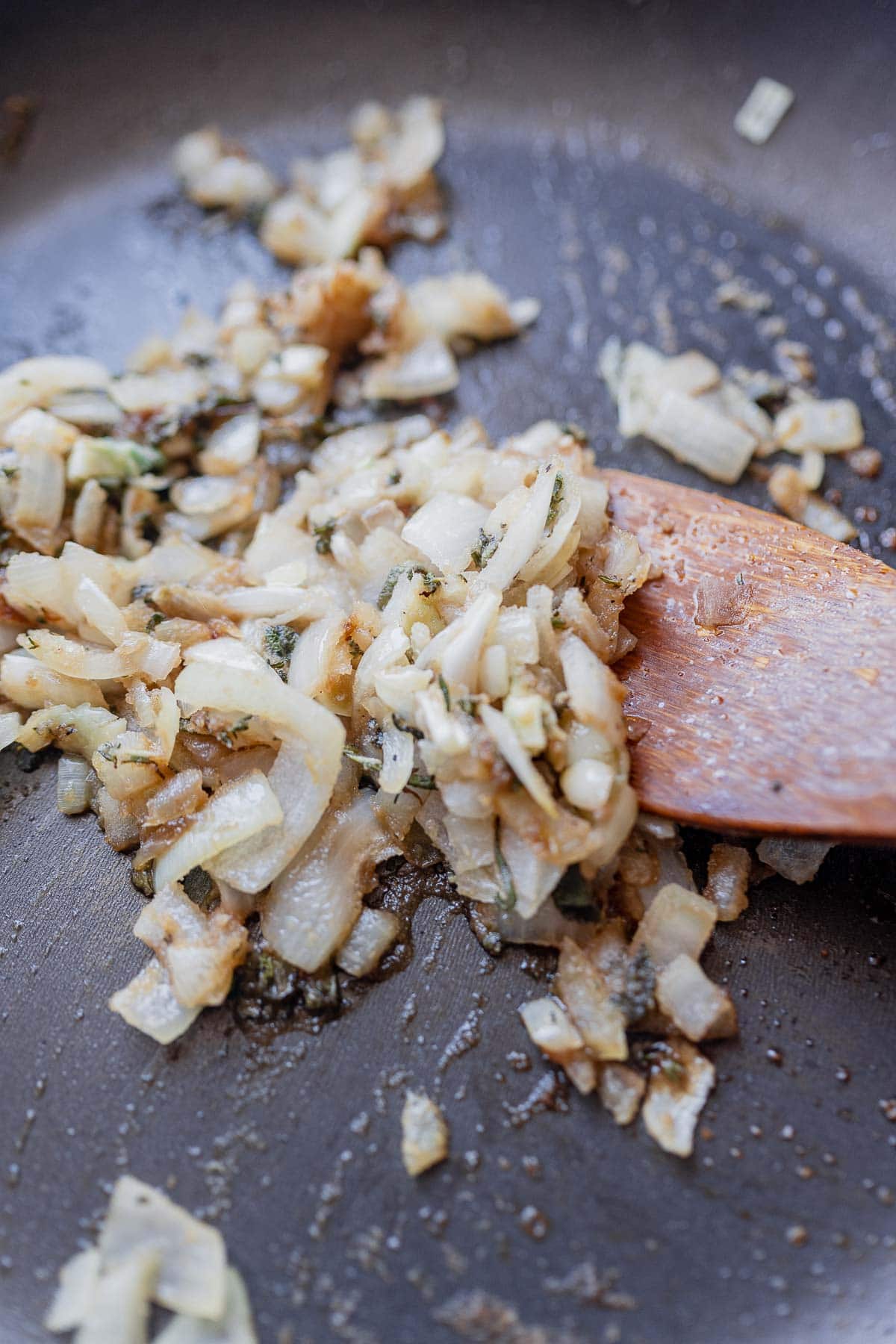 A wooden spoon moves sautéed veggies in a skillet.