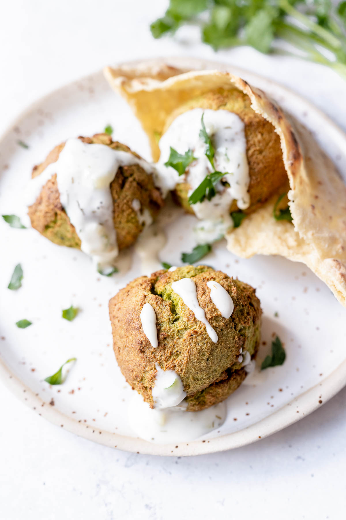 A close shot of falafel drizzled with tzatziki resting on a white ceramic plate.