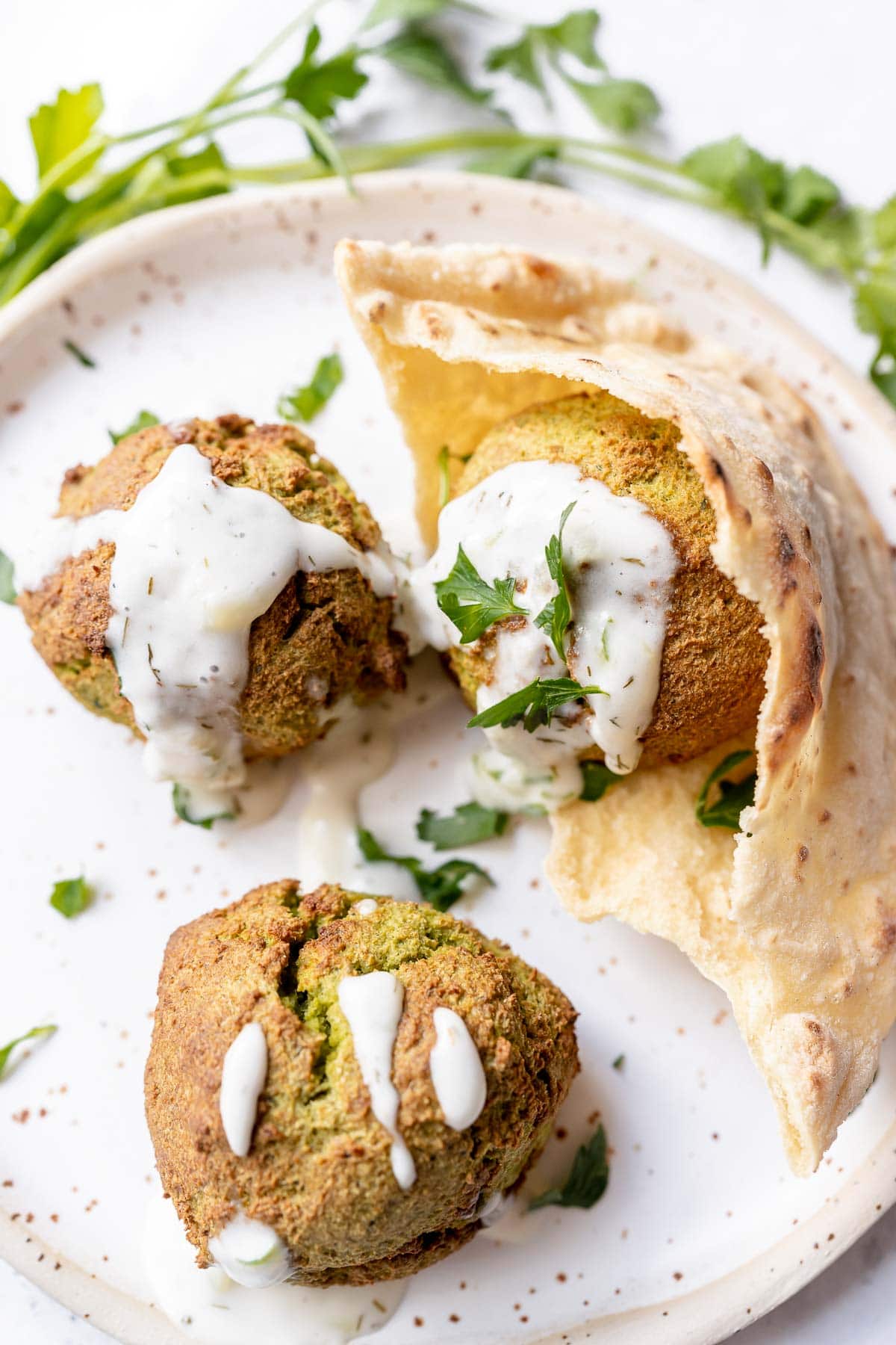 Crispy falafel stuck in white pita bread drizzled with sauce and topped with fresh green herbs.