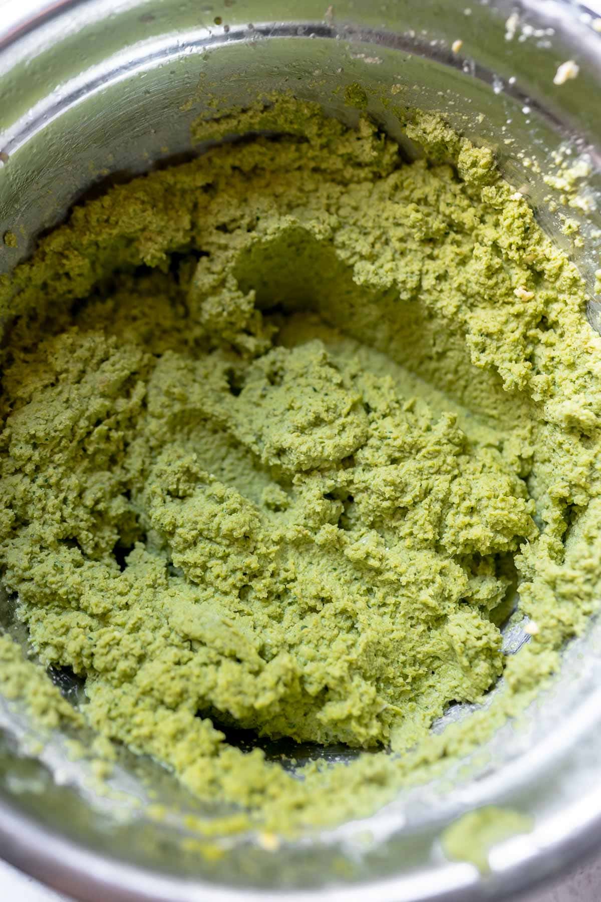 A silver mixing bowl filled with green falafel batter.