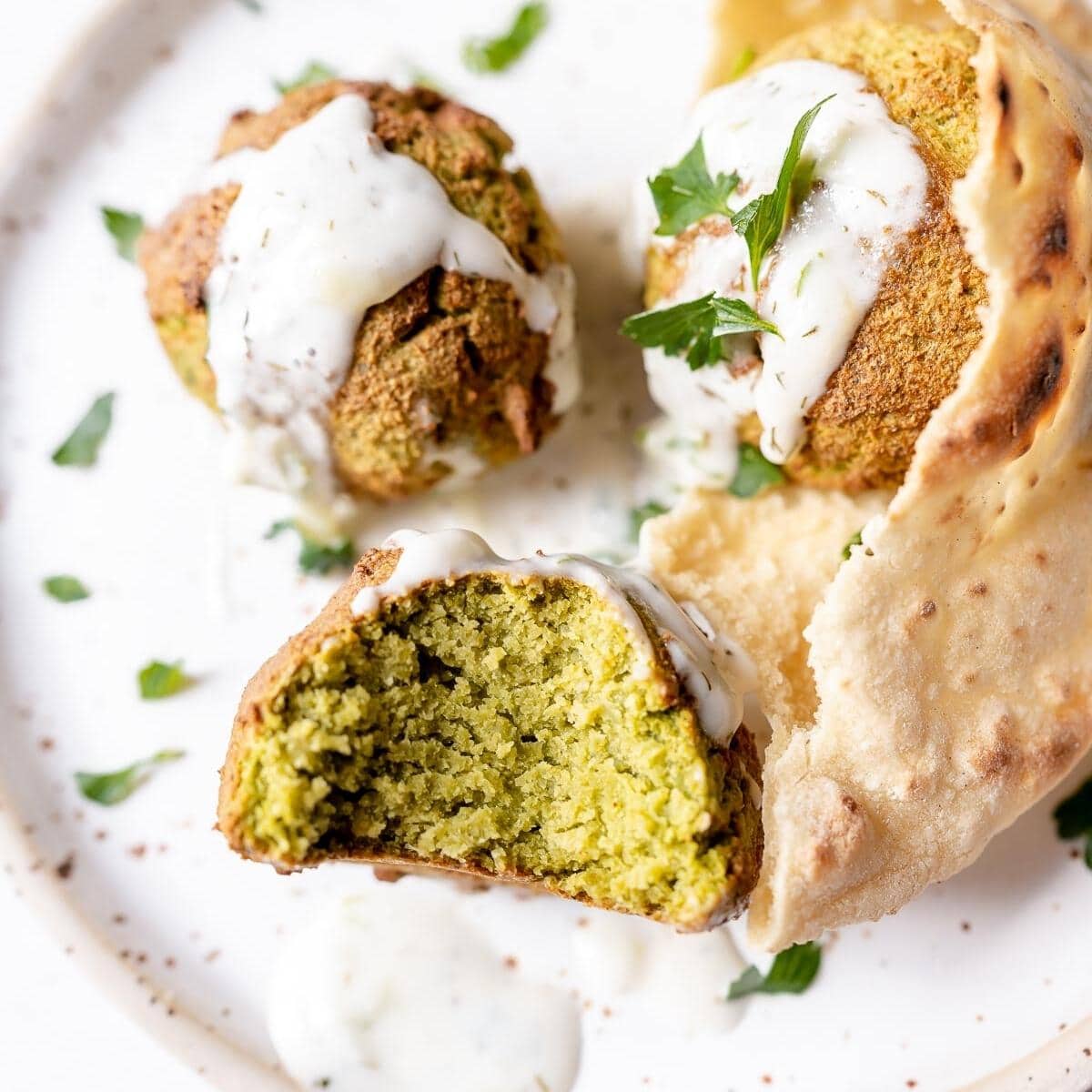 A close shot of a falafel ball with a bite taken out of it revealing its green insides.