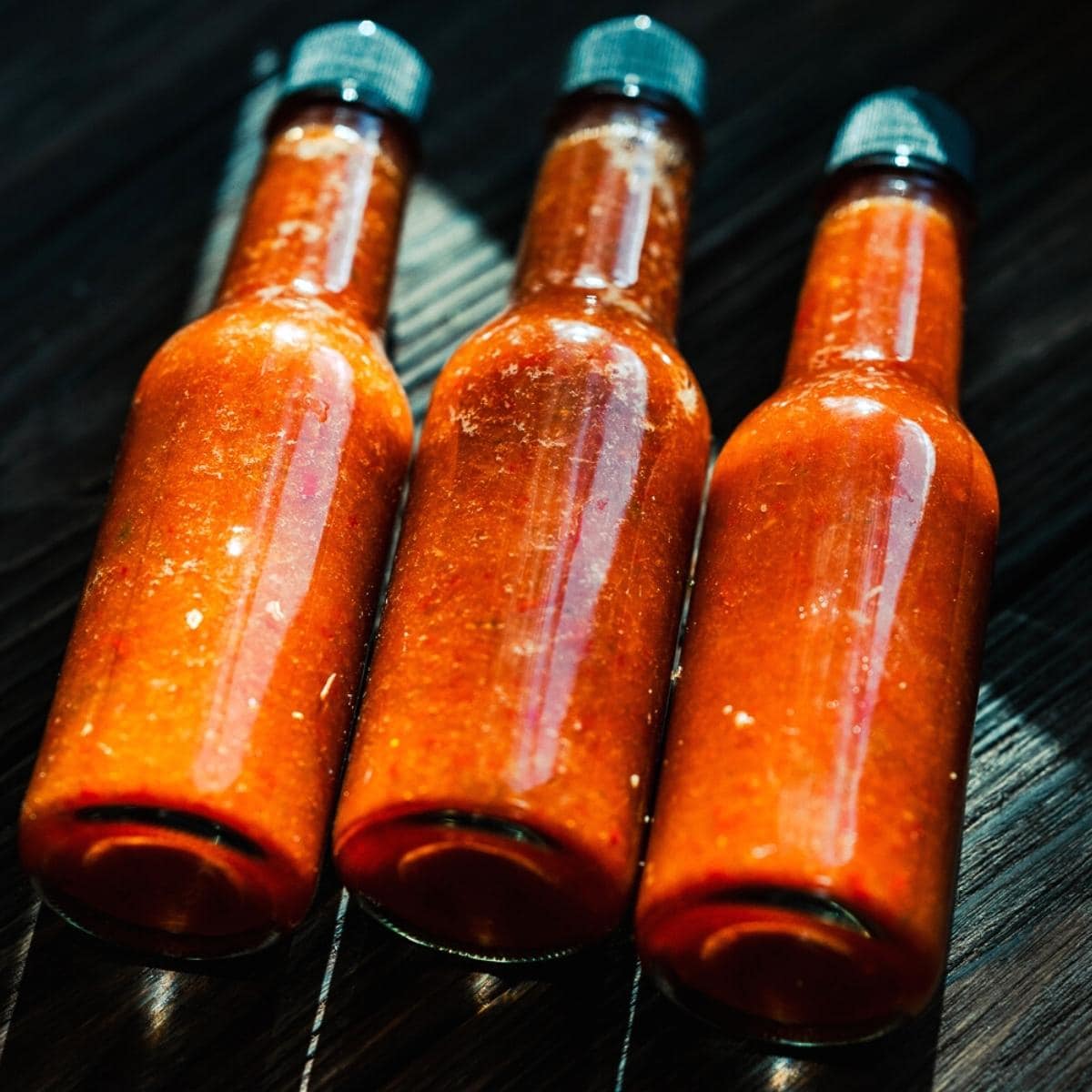 3 glass bottles of red hot sauce glistening in the afternoon sun.