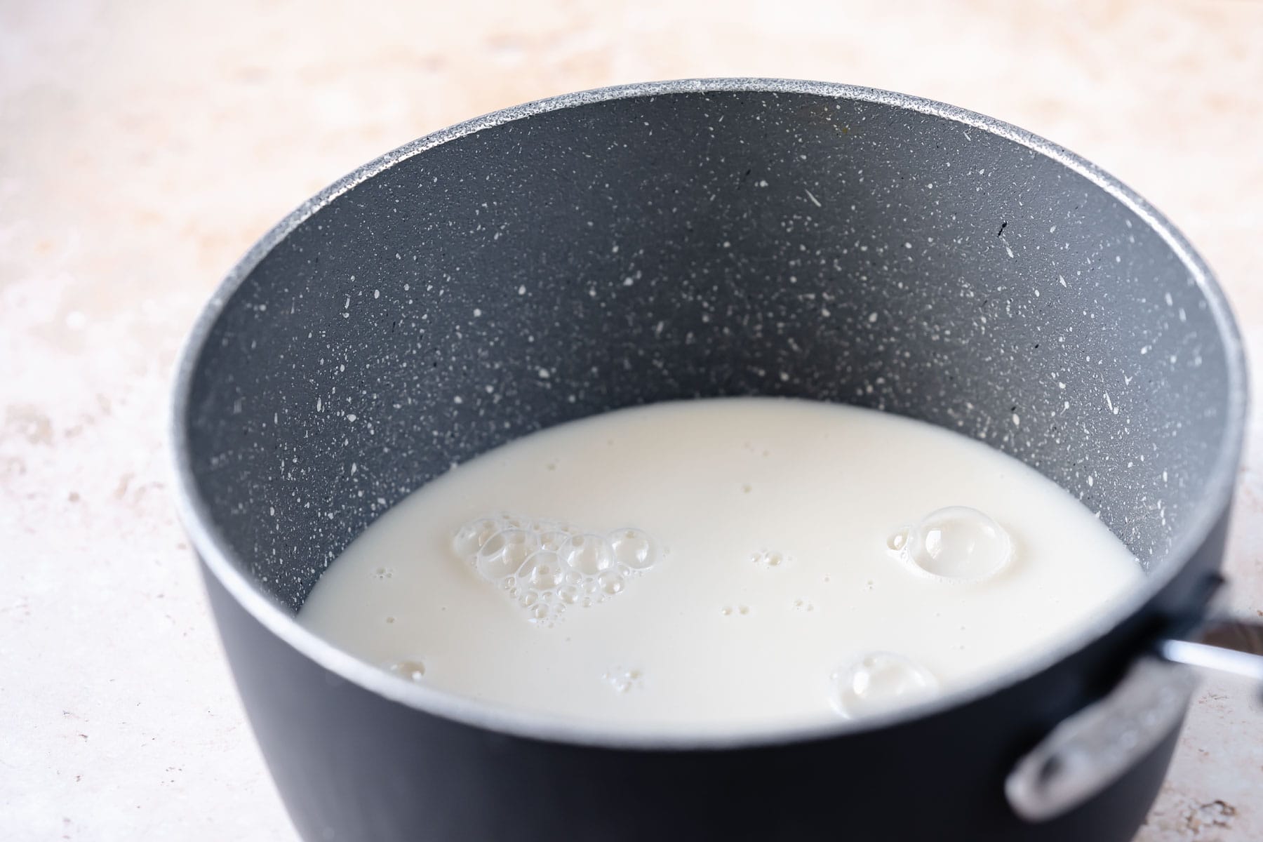 A dark gray saucepan filled with a white liquid.
