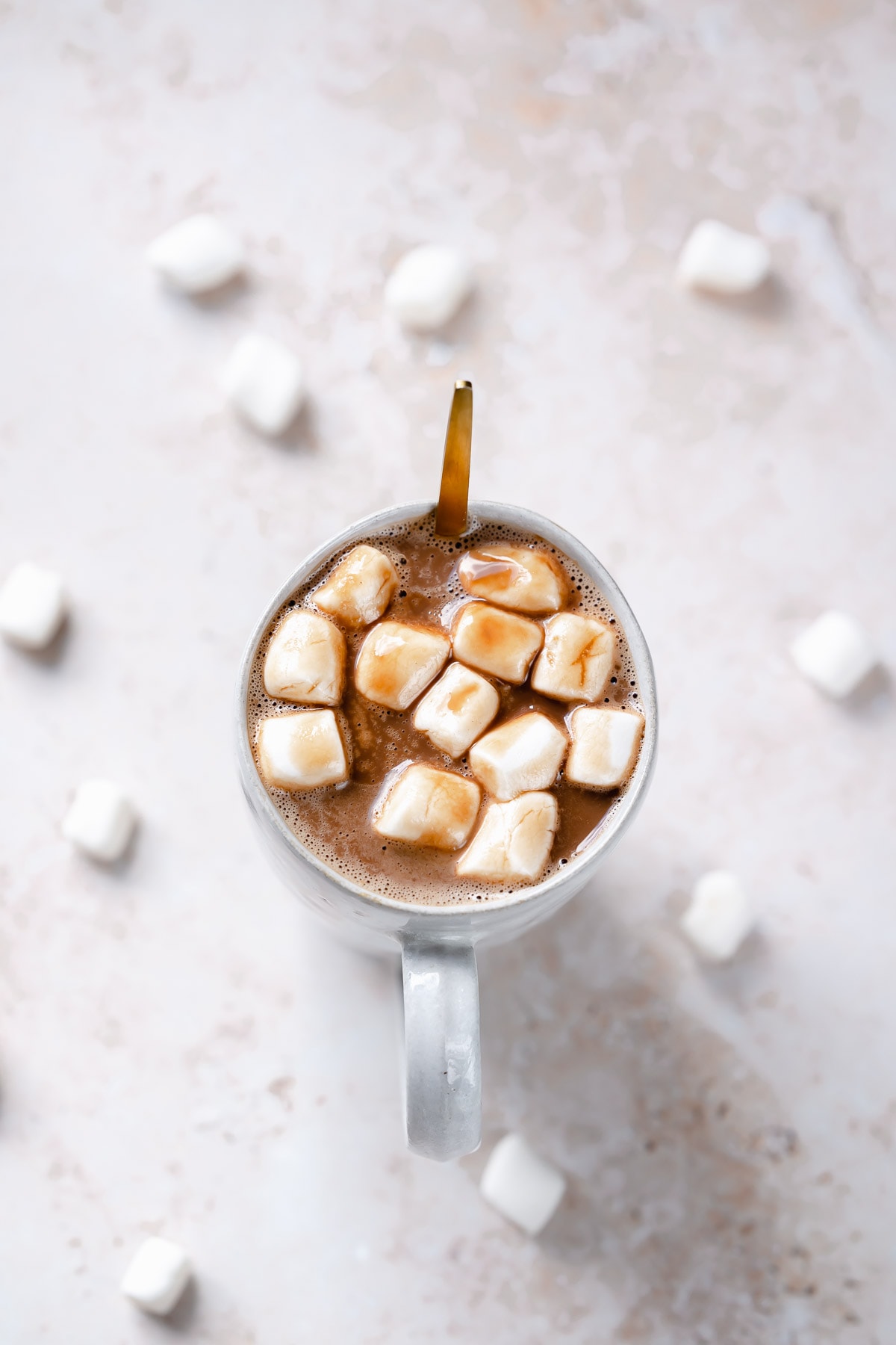 A gold spoon sticks out of a ceramic mug filled with vegan hot chocolate.