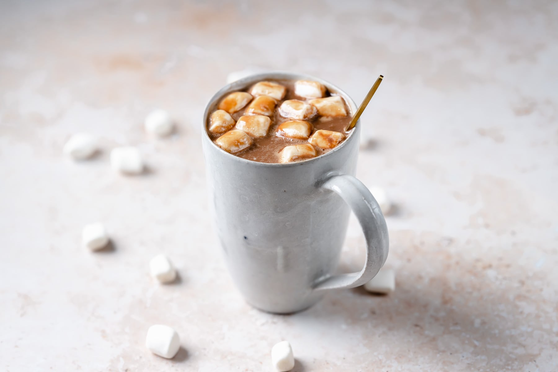 A golden spoon stick out of a white ceramic mug filled with hot chocolate.