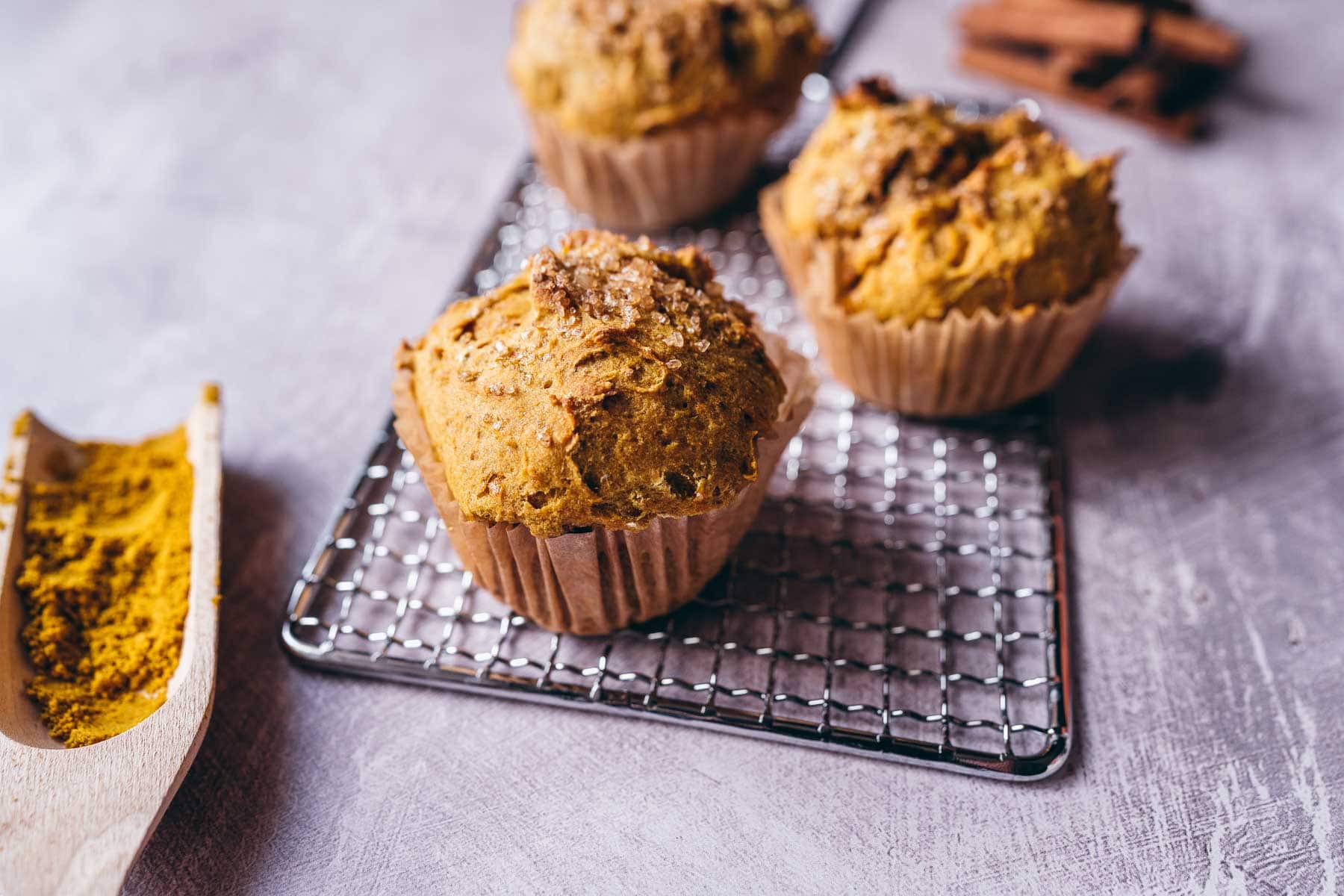 Golden muffins resting on a silver cooling rack.