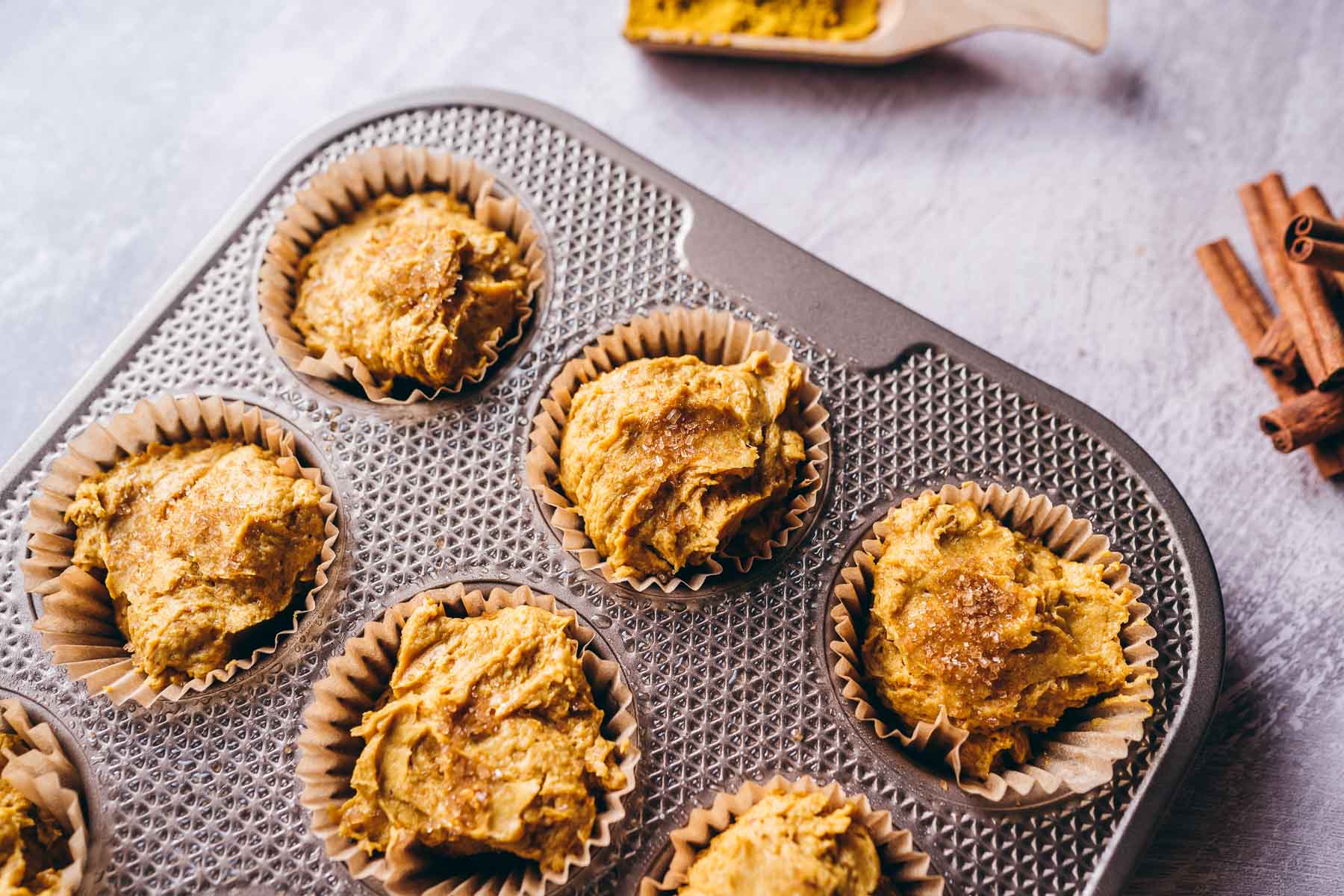 A dark silver muffin tin filled with unbaked muffin batter.