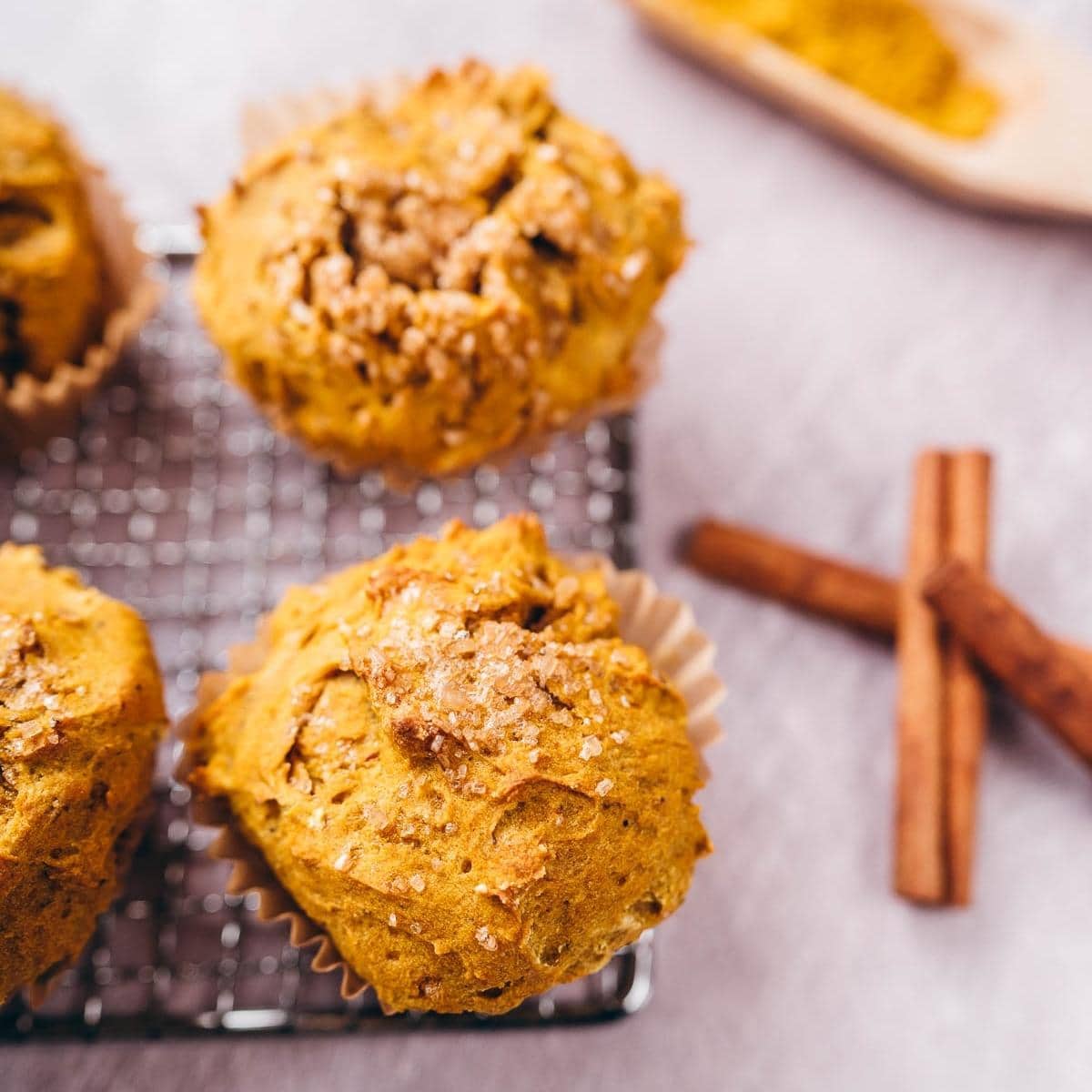 Gold muffins with a crunchy sugar topping resting on a silver metal rack.