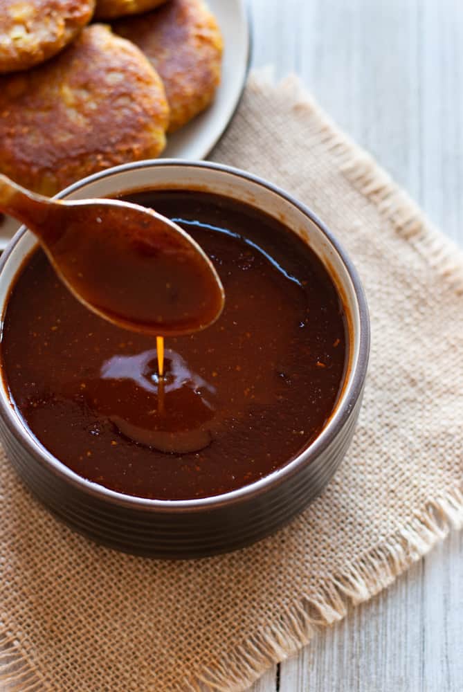 Homemade tamarind chutney dripping from a wooden spoon.