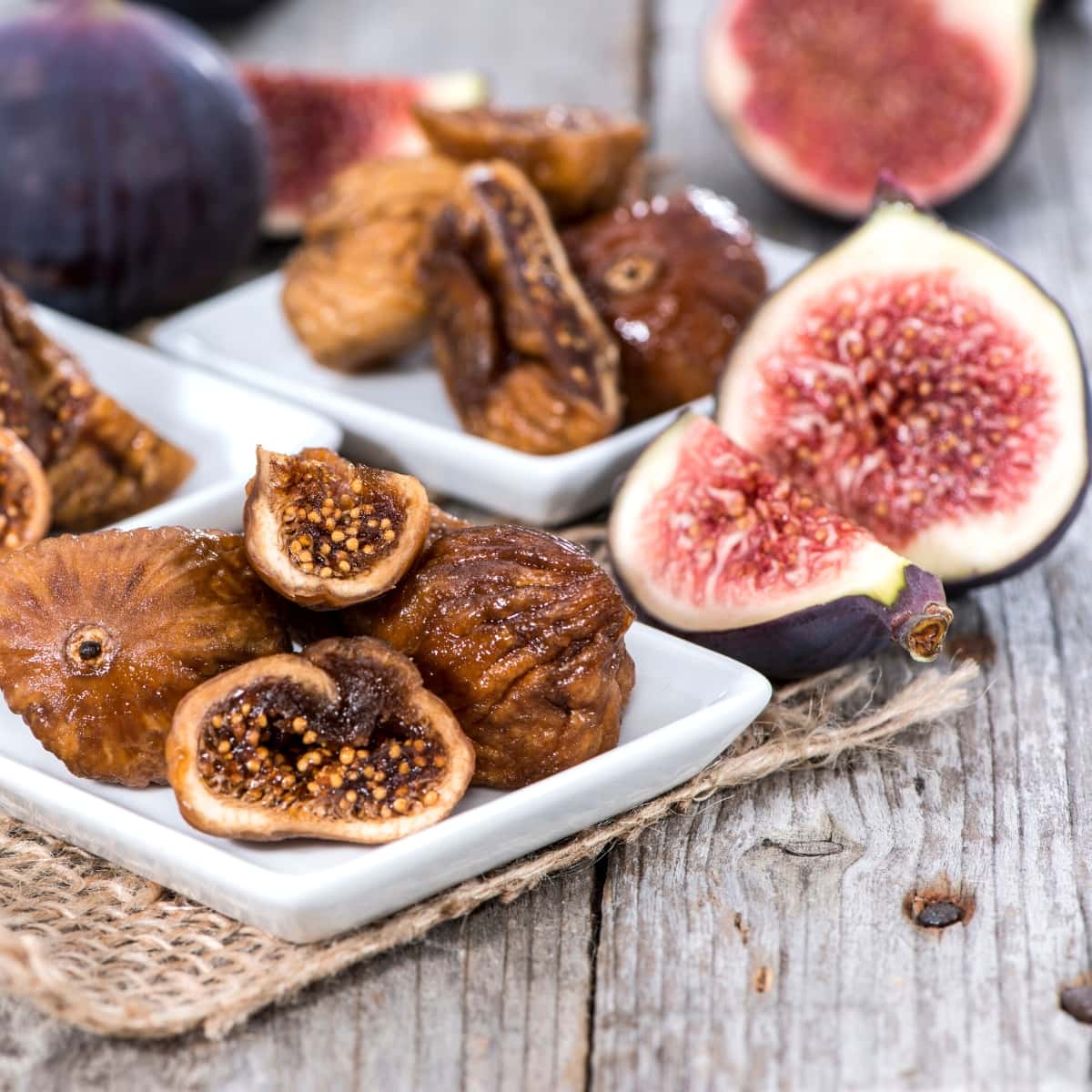 Fresh and dried figs resting on white plates on a wooden table.