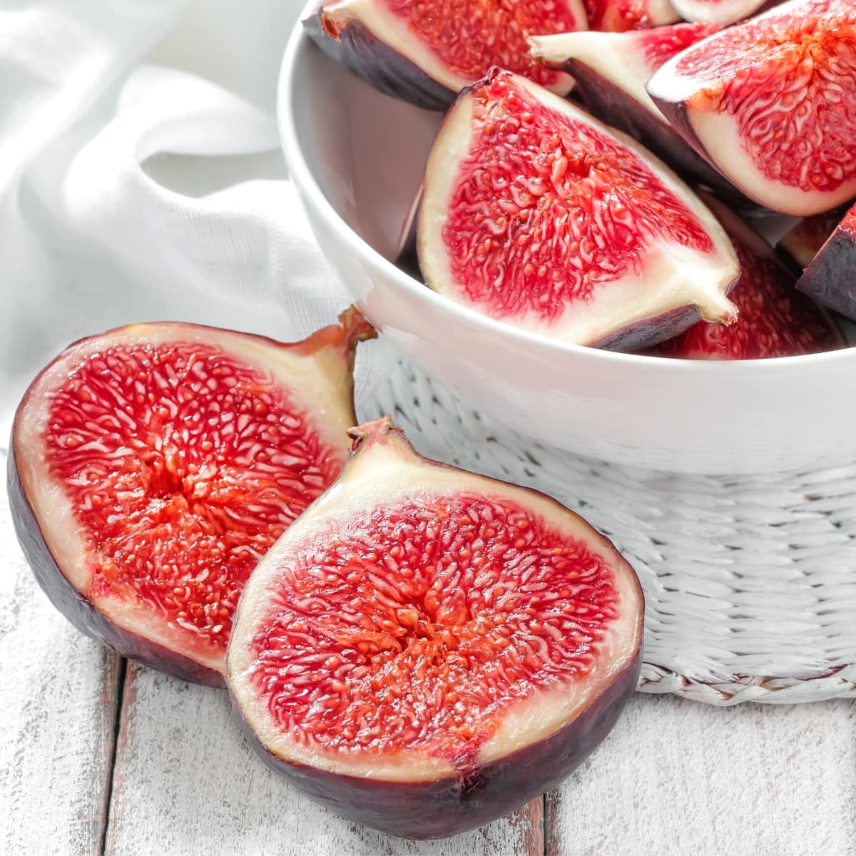A white bowl filled with vibrant pink and purple sliced fresh figs.