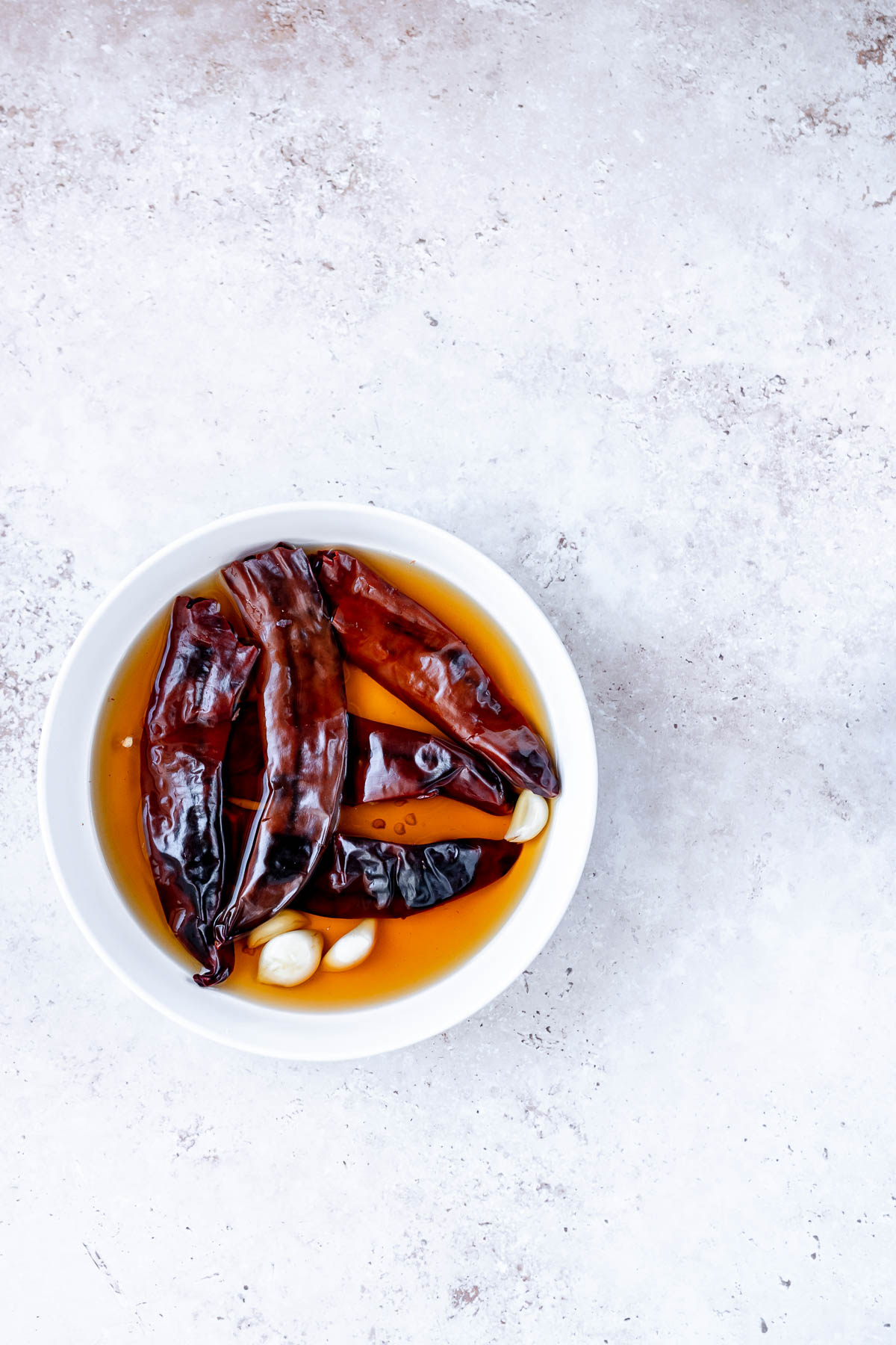 A white bowl filled with chiles, garlic and water.