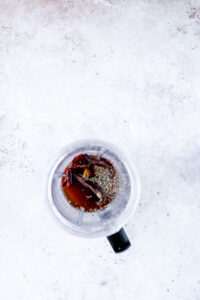 Overhead view of a blender containing Guajillo Sauce ingredients, including dried chilies, spices, and liquid, on a light textured surface.