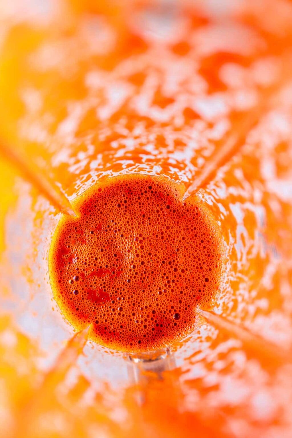 Top view of a blender containing bright orange liquid with visible bubbles, likely a Guajillo Sauce or juice, against the transparent sides of the blender jar.