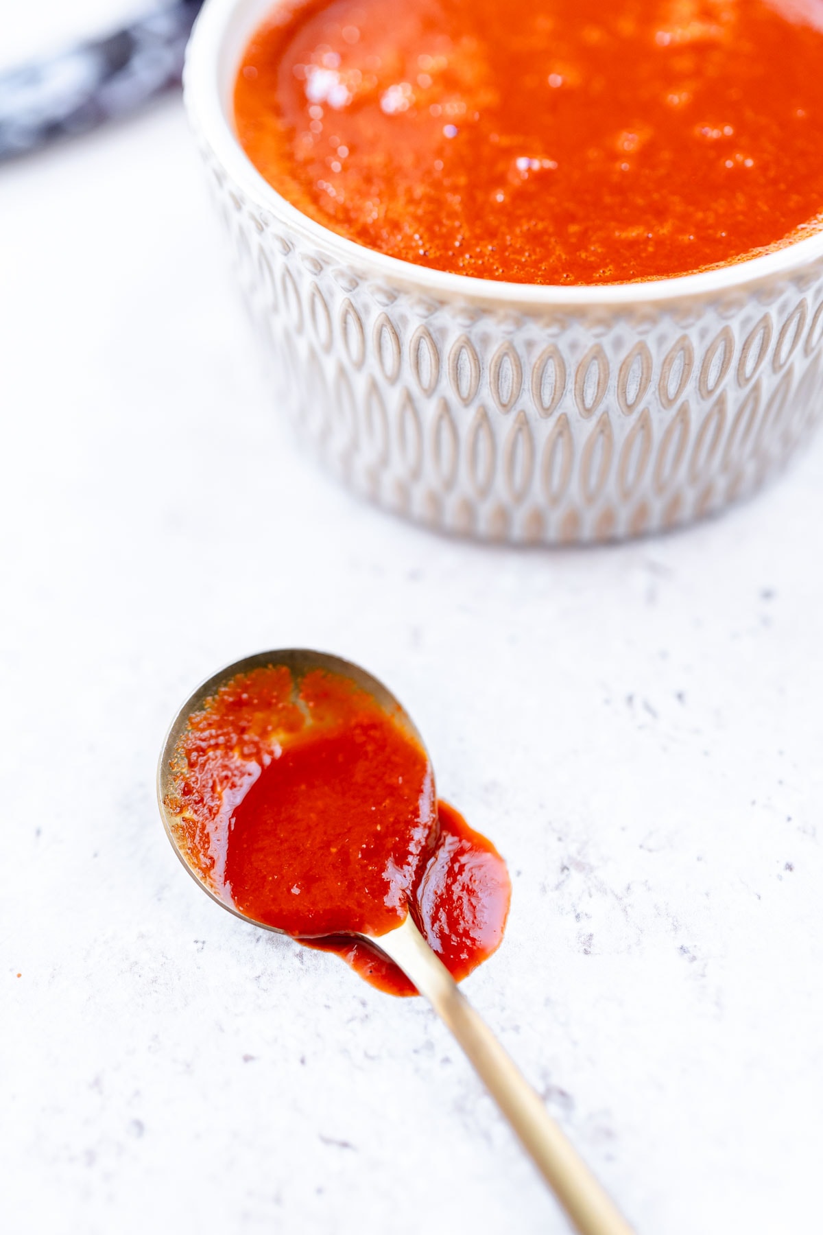 A gold spoon dripping with red sauce rests on a white table.