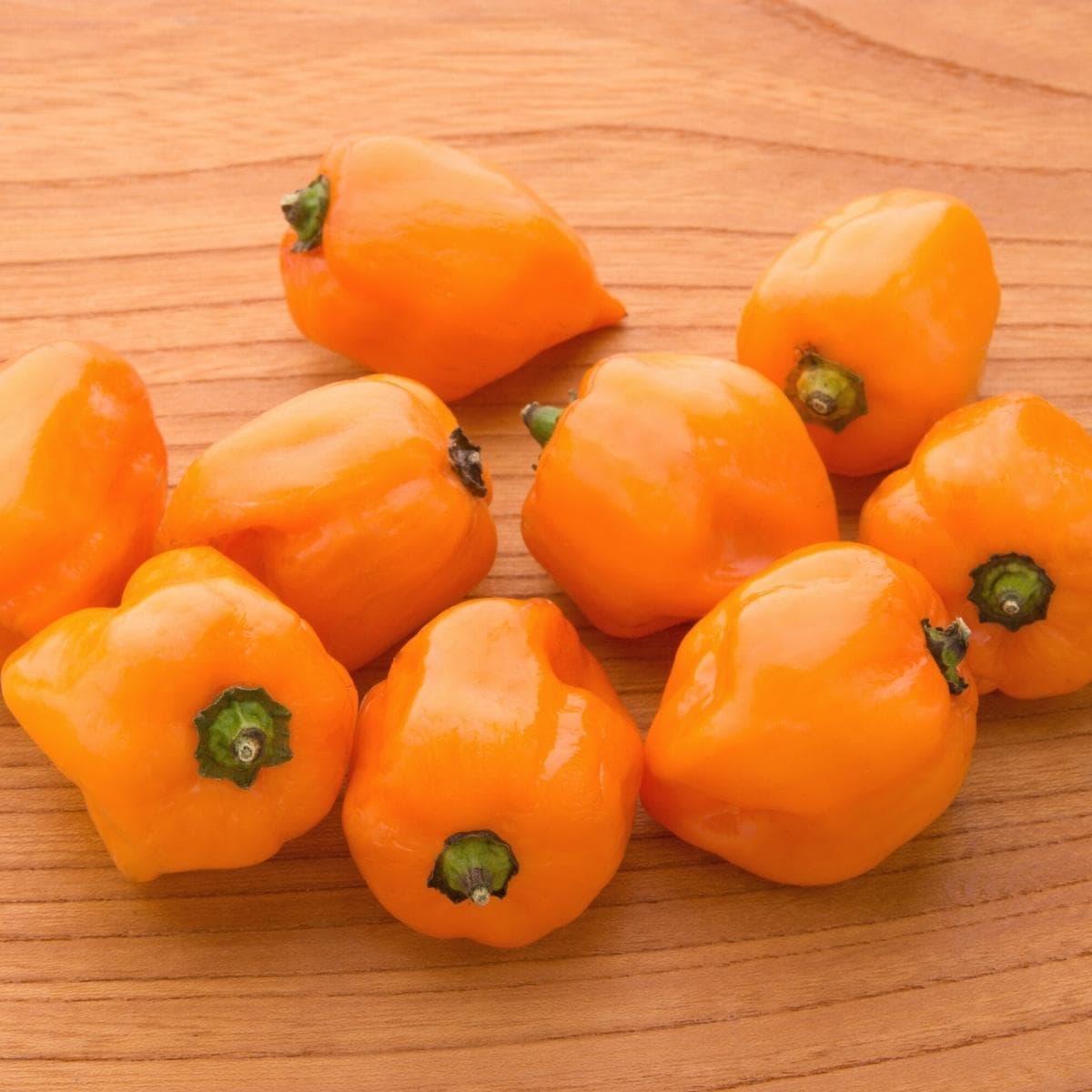 Orange habanero peppers resting on a wooden table.