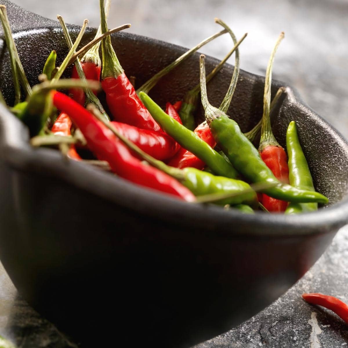 A black bowl filled with red and green Thai chili peppers.