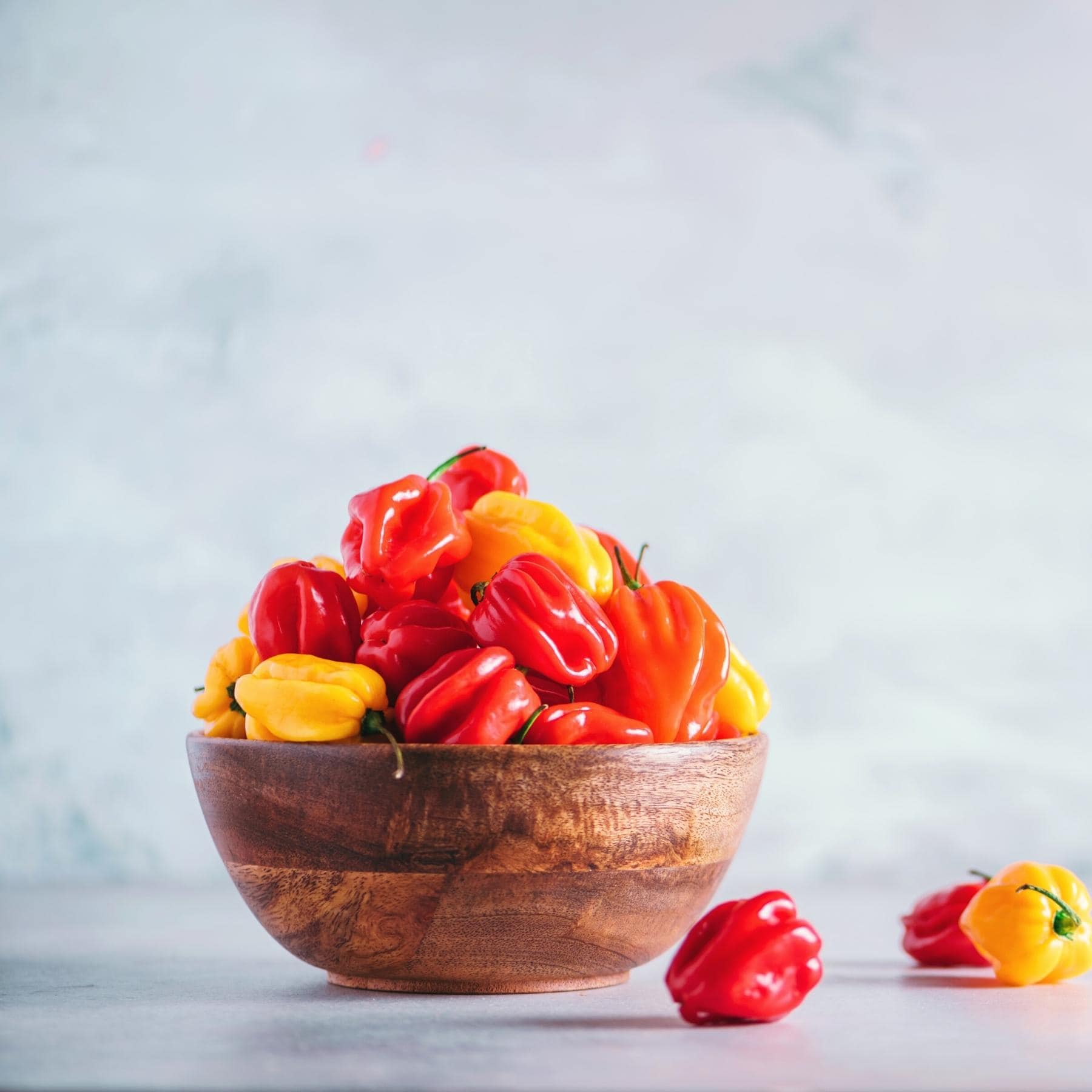 A wooden bowl filled with fresh, colorful scotch bonnet peppers.