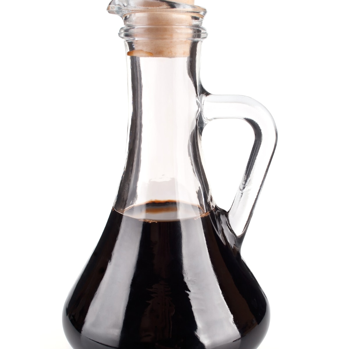 A clear glass corked container filled with dark brown balsamic vinegar.