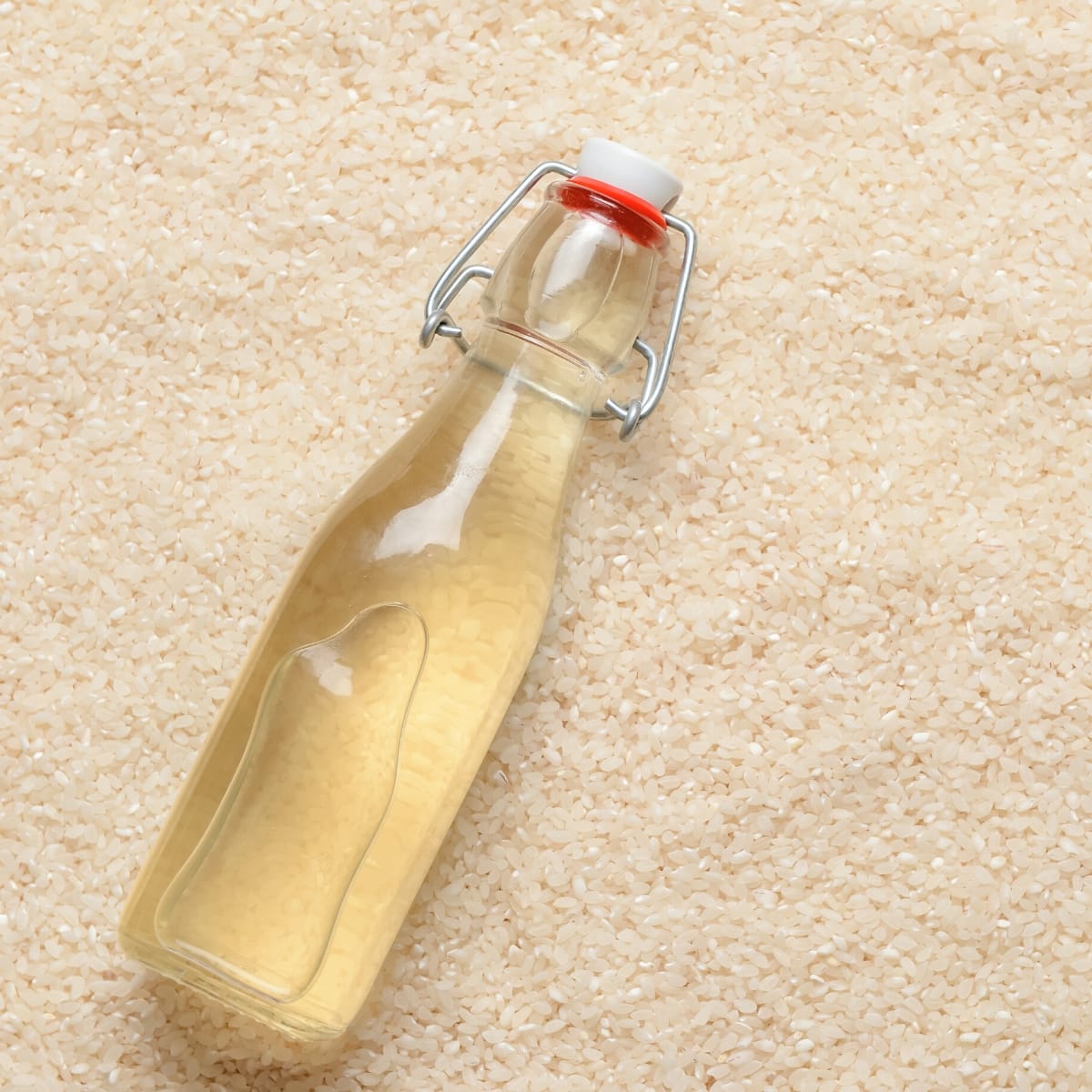 A clear glass bottle filled with rice vinegar resting on white rice.