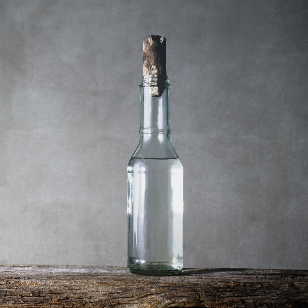 A tall slender glass bottle filled with clear white vinegar.