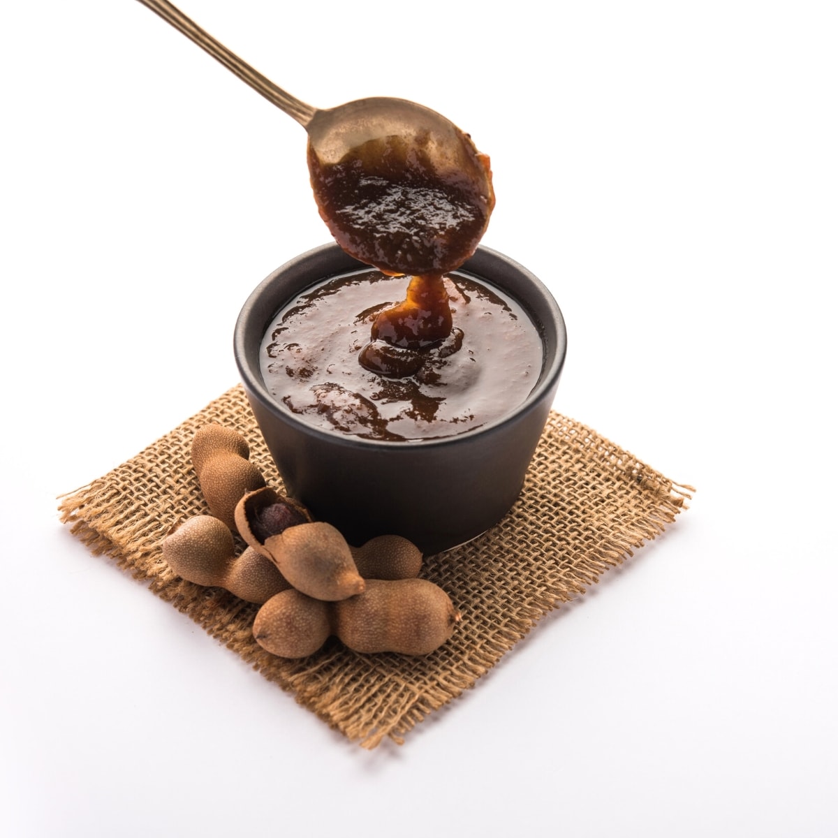 A silver spoon dipping into a small bowl of dark brown tamarind paste.
