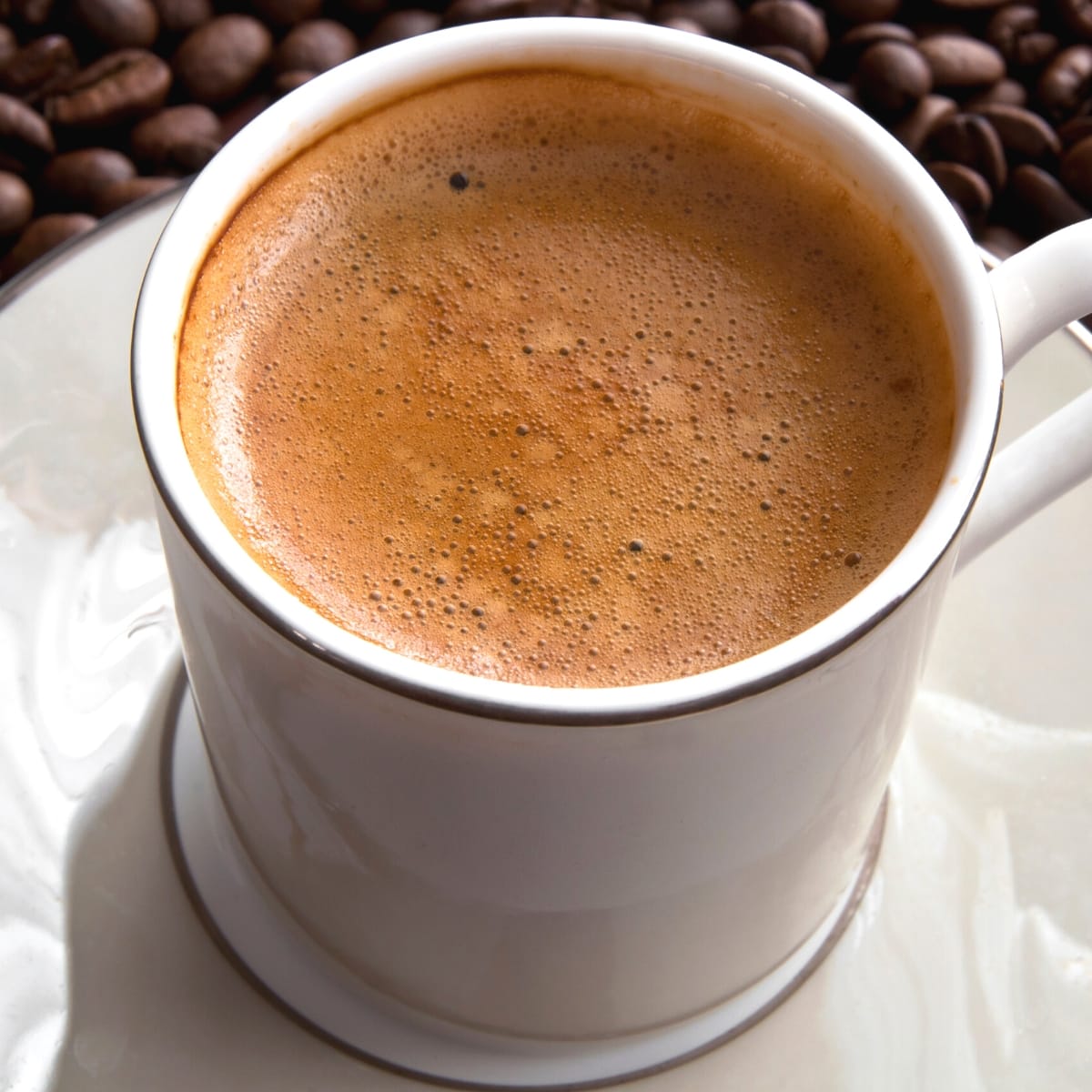 A white ceramic mug filled with frothy cuban coffee.