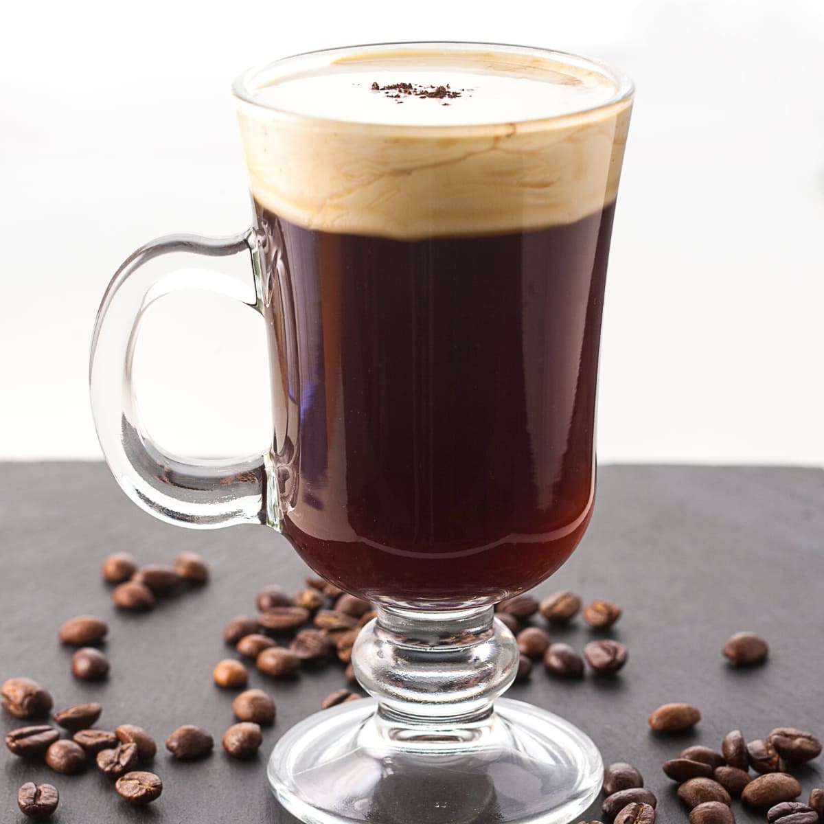 A tall handled glass mug filled with Irish coffee.