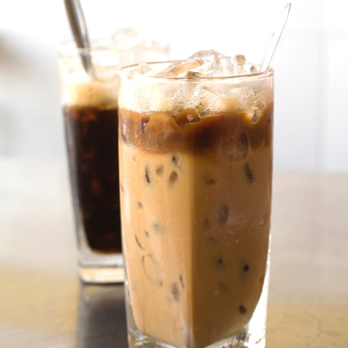 Two tall clear glasses filled with iced coffee.