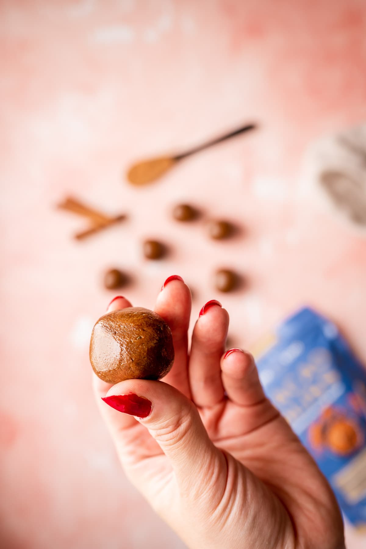 A hand with red painted nails holds a chocolate sunbutter bite close to the camera.