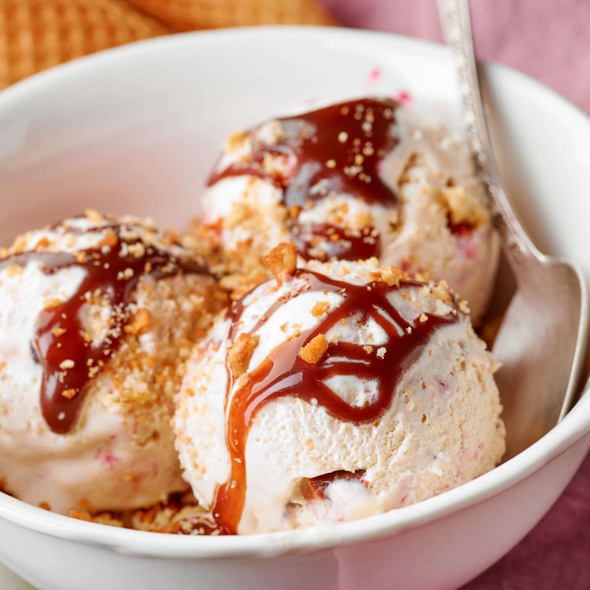 A white bowl filled with white ice cream drizzled with brown caramel sauce and sprinkled with crushed cookies.