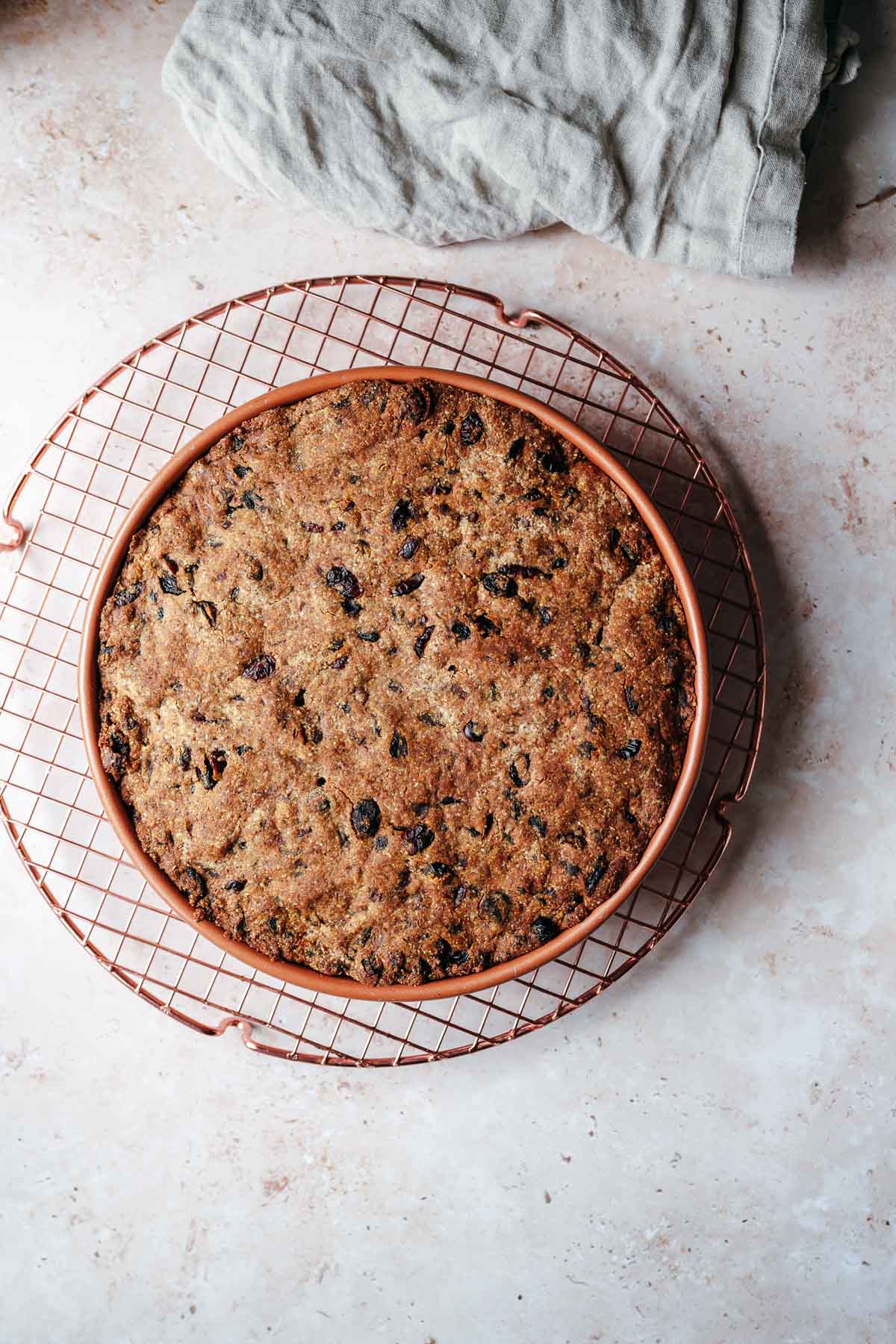 A freshly baked fruit cake on a bronze cooling rack.