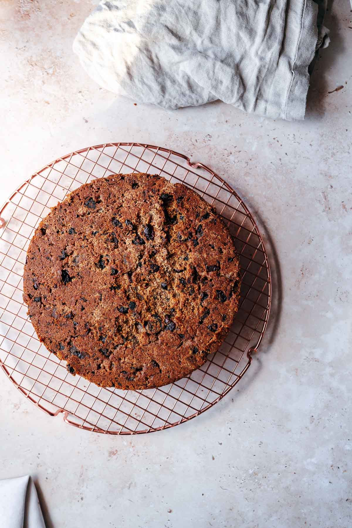 An upside down fruit cake on a bronze cooling rack.