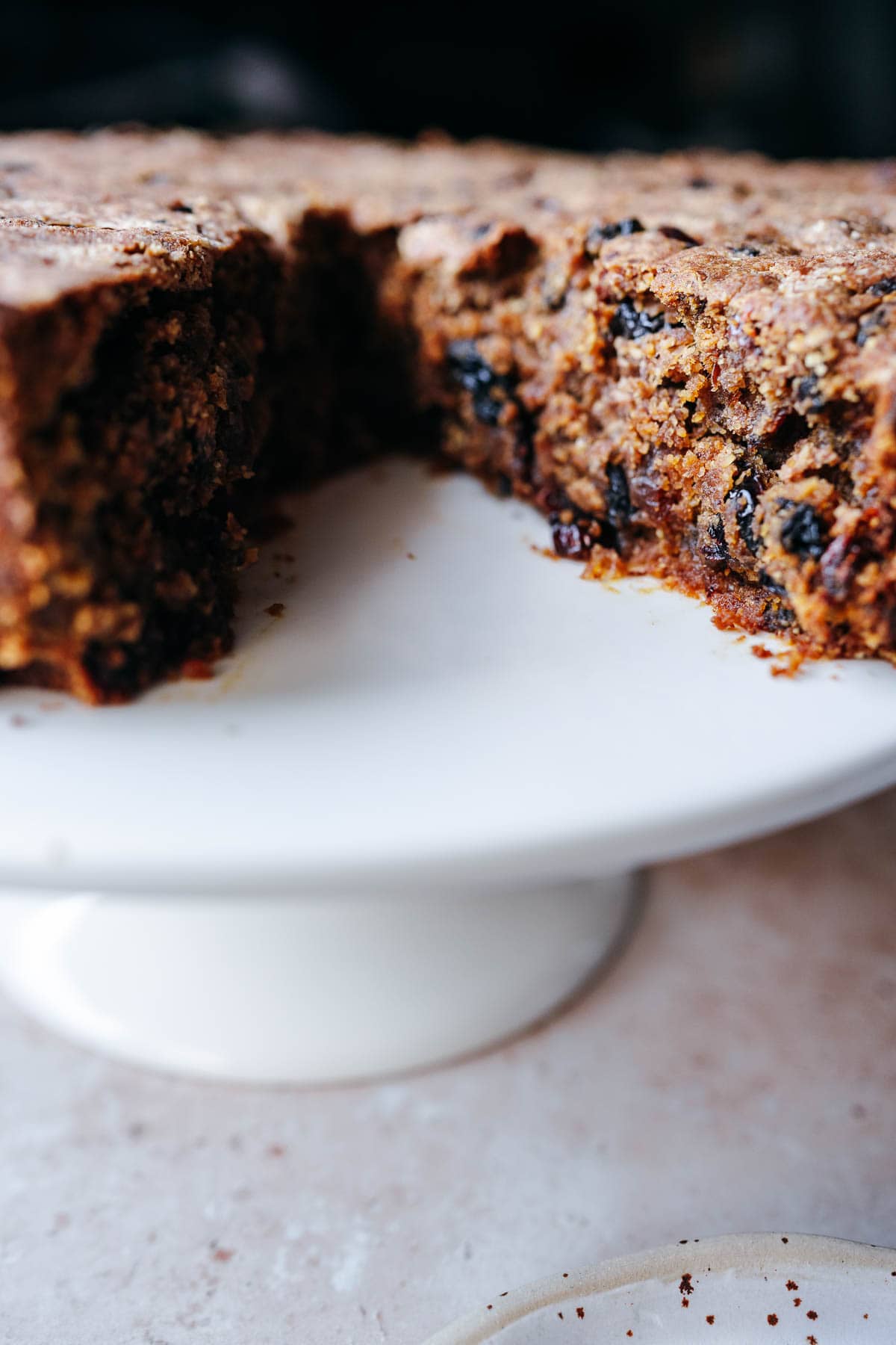 Close shot of sliced gluten free fruit cake on white ceramic cake stand.