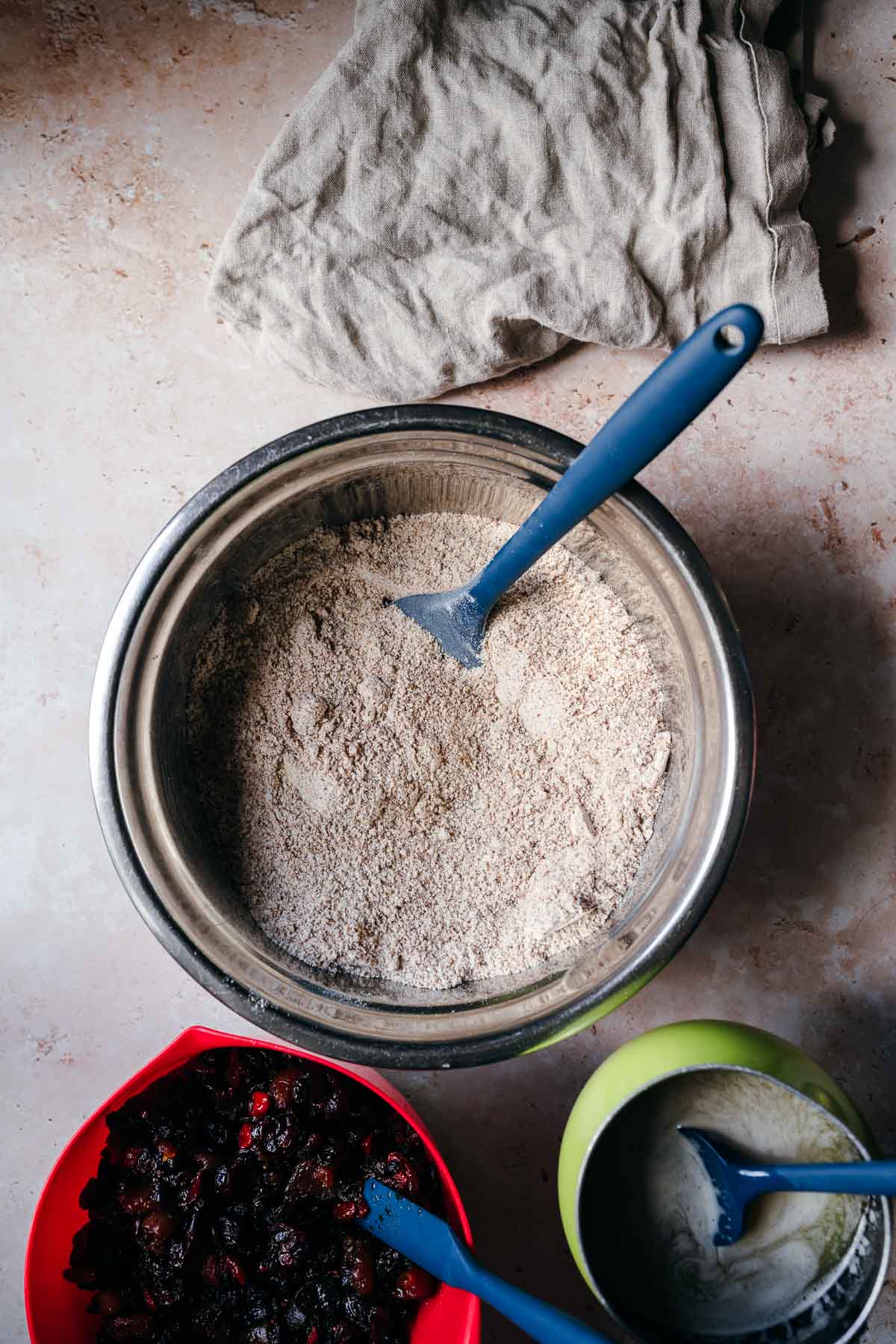 A bowl of flour and spices, a bowl of dried fruit and a pan of melted butter resting together.