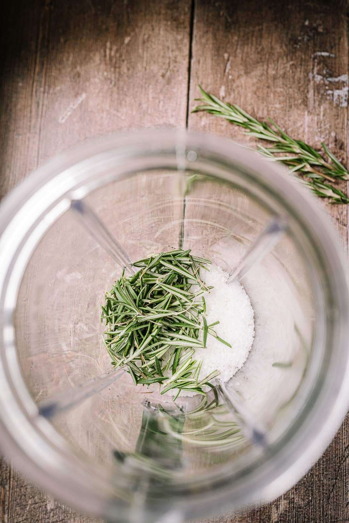 A blender container filled with rosemary leaves and salt.