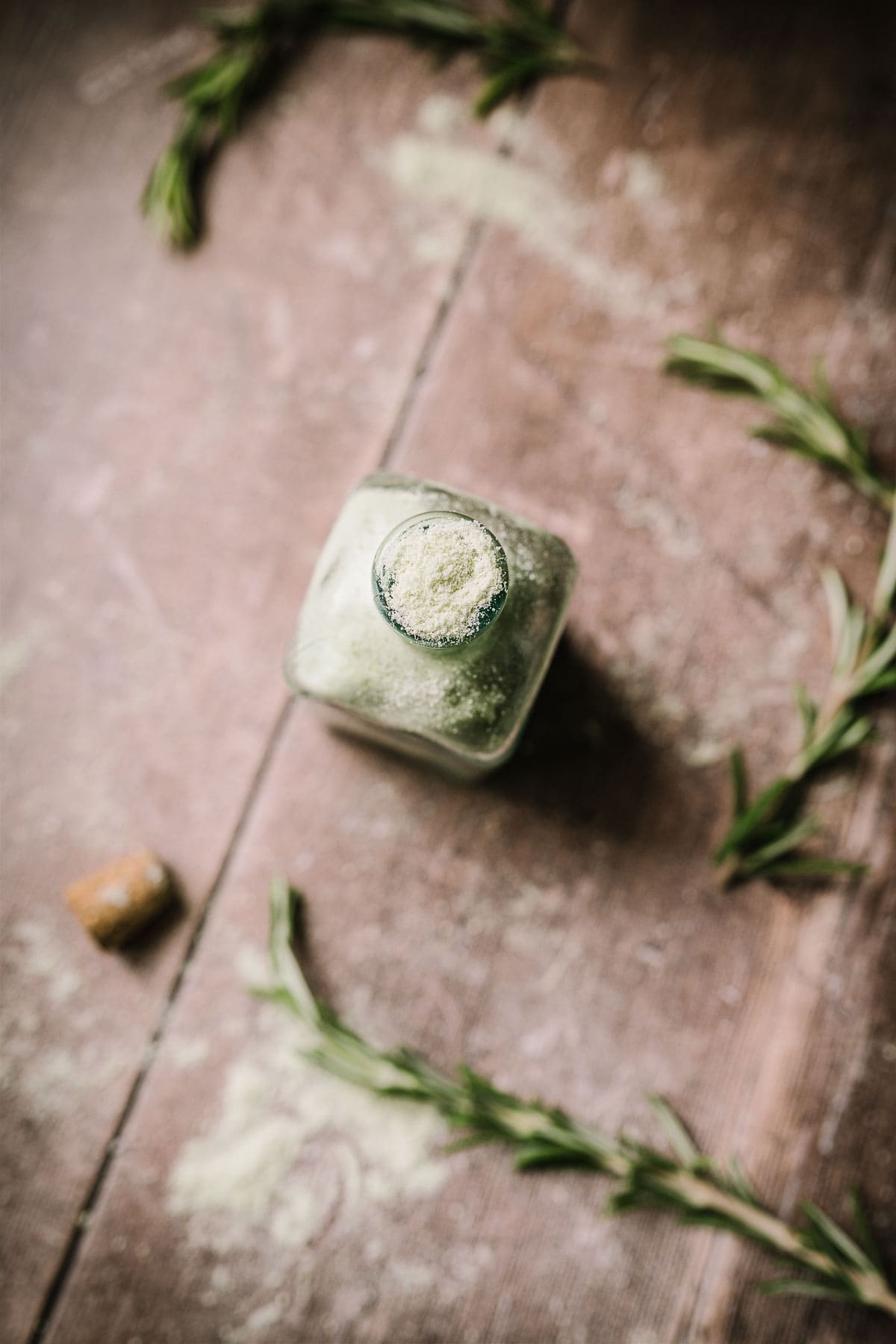 Close shot of top view of open glass bottle filled with green rosemary salt.