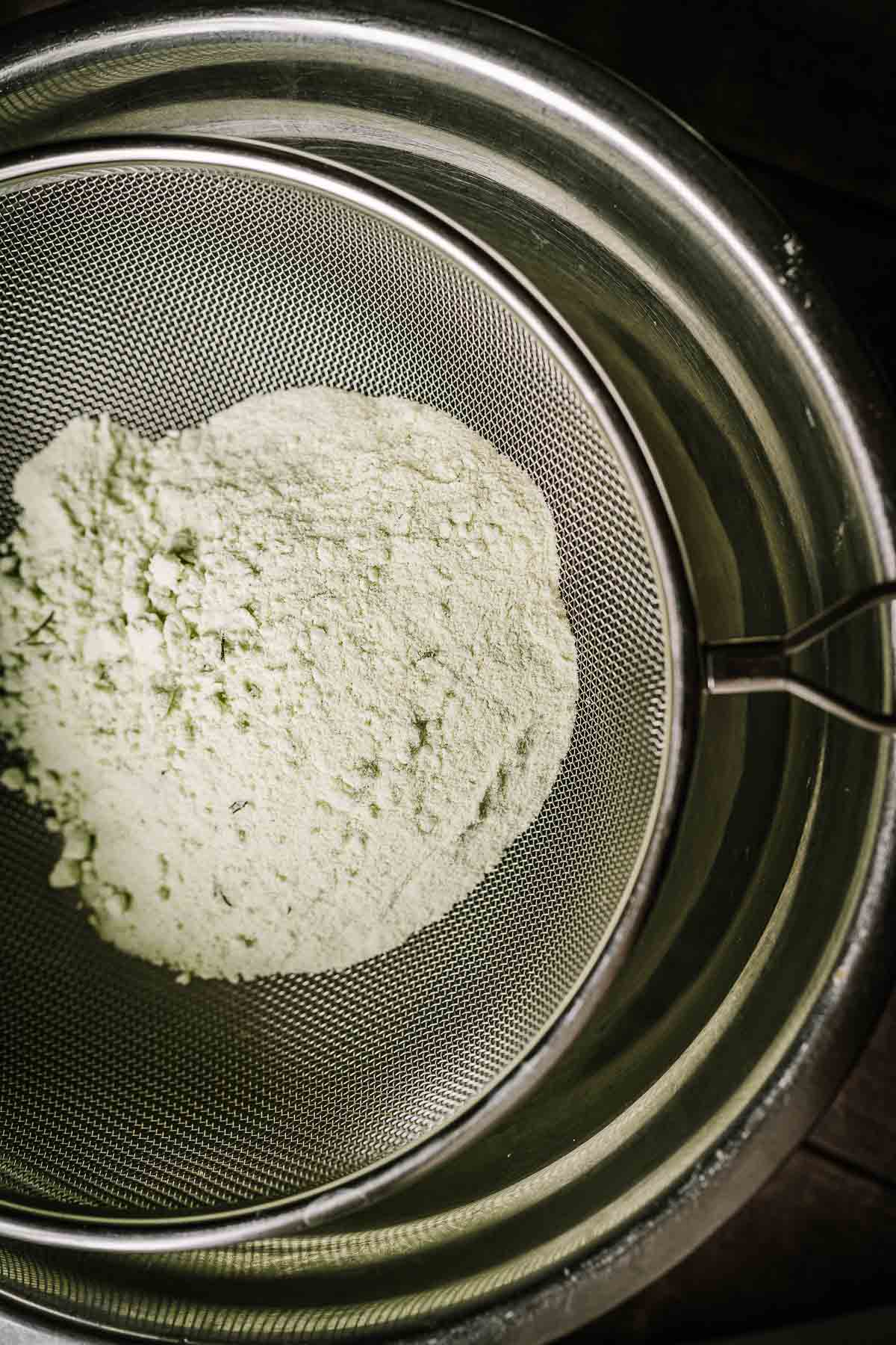 A metal mesh strainer filled with light green salt.