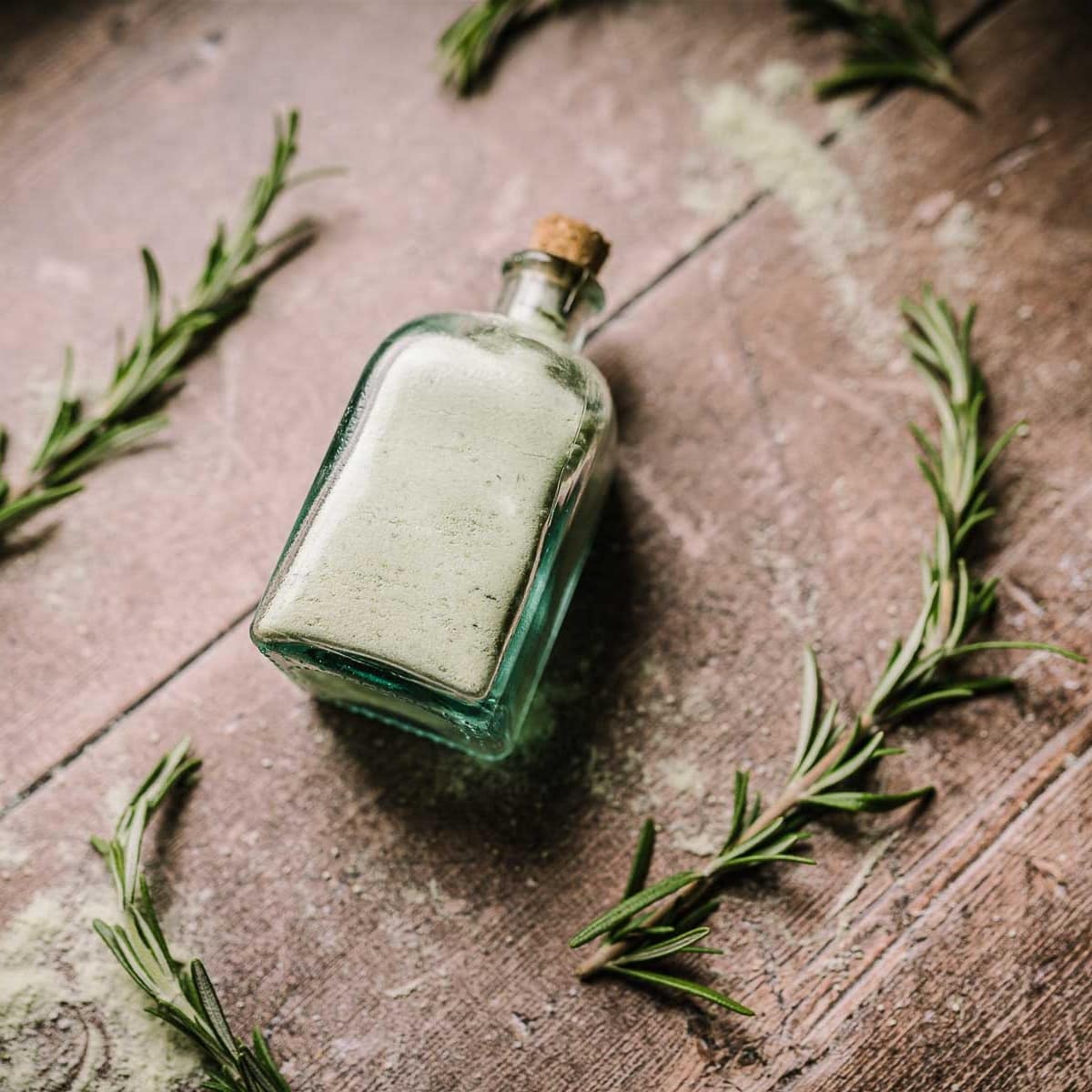 A clear glass bottle filled with green salt and closed with a small cork.