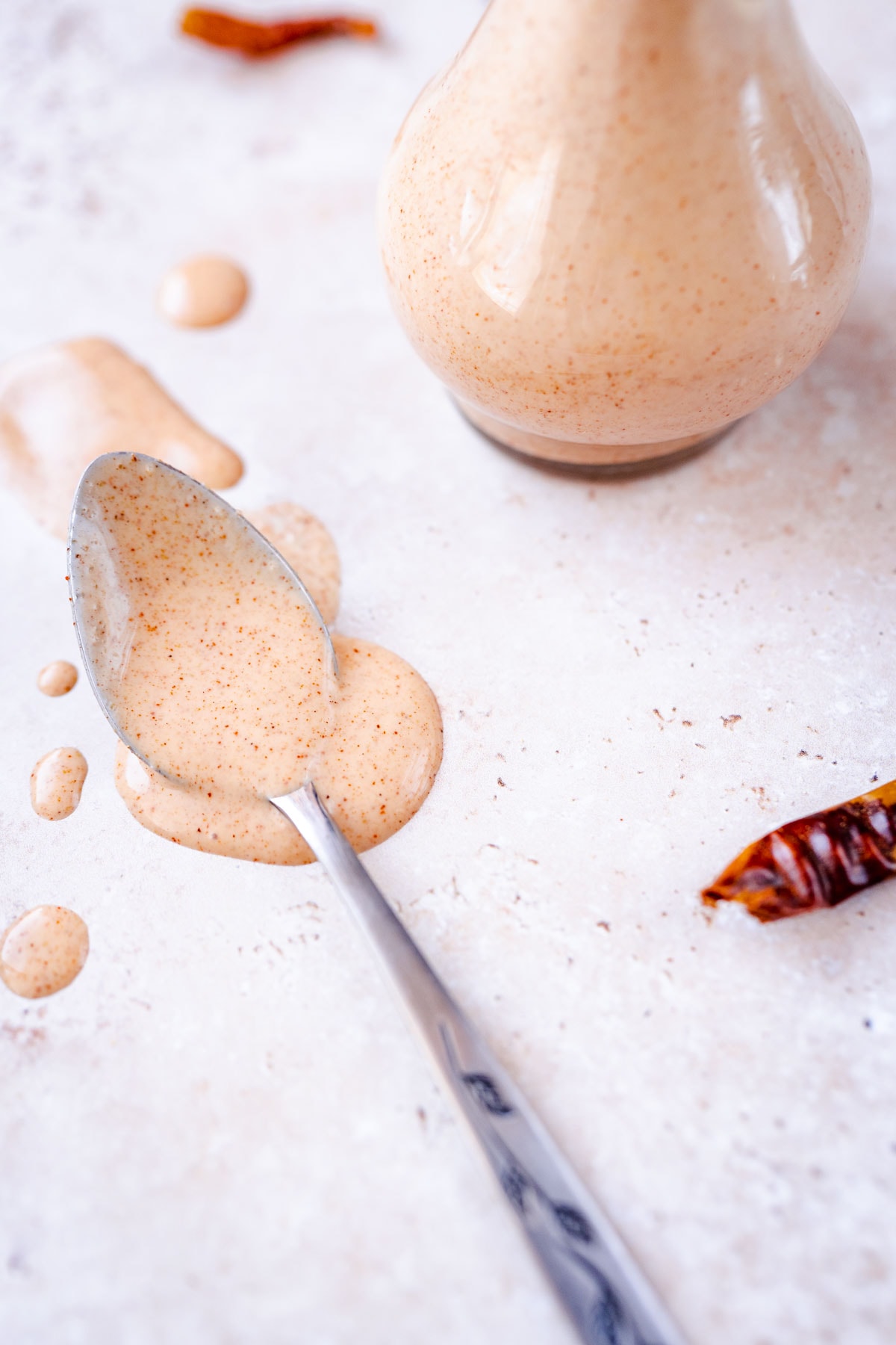 Close shot of a silver spoon dripping with light orange salad dressing.