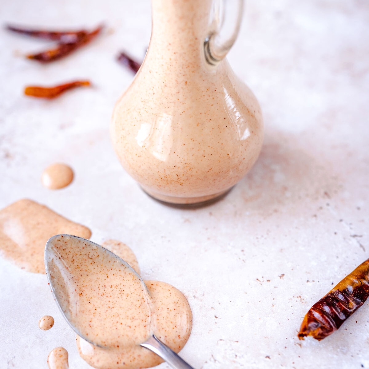 A silver spoon filled with homemade salad dressing resting on a white table next to a red dried chile.