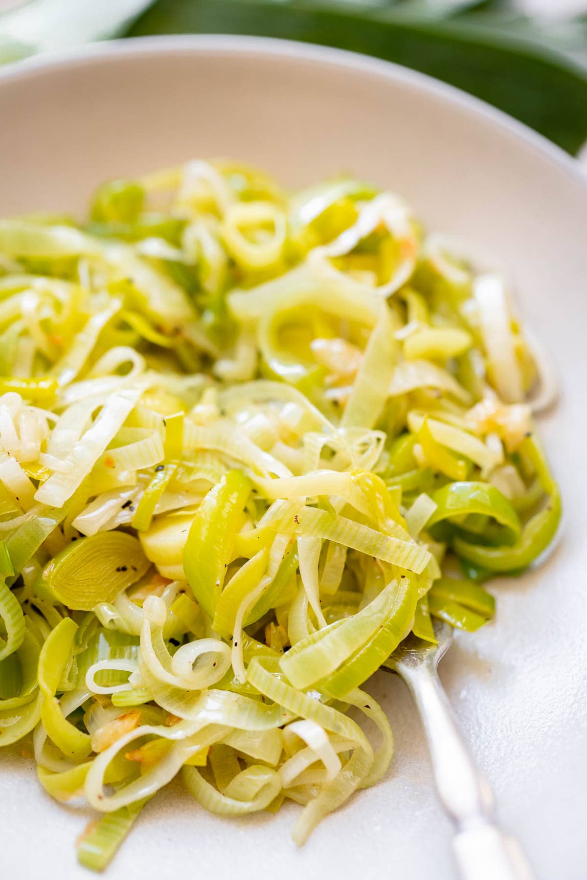 Close shot of a silver fork holding a forkful of sliced leeks in a bowl.